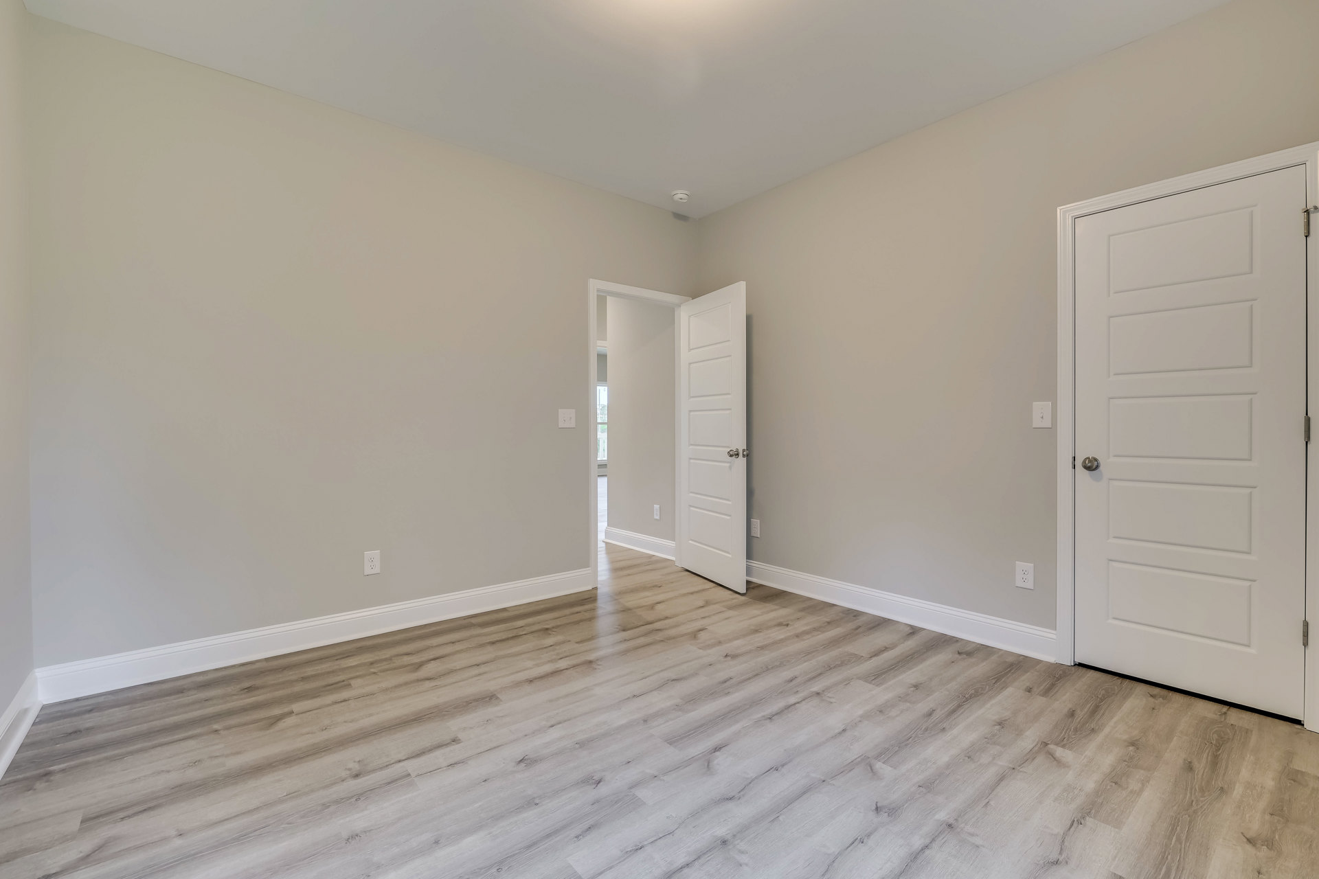 White paneled door with silver knob open to a room featuring light wood flooring, white walls, and white baseboard trim
