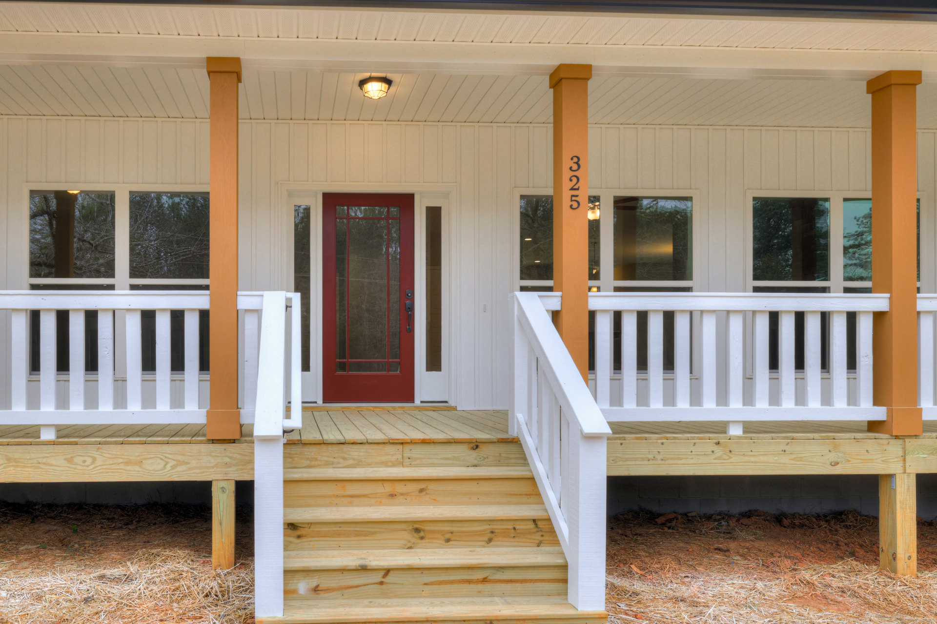 Front porch with wooden stairs and white railing, red door with glass panels, ceiling light fixture, exterior windows