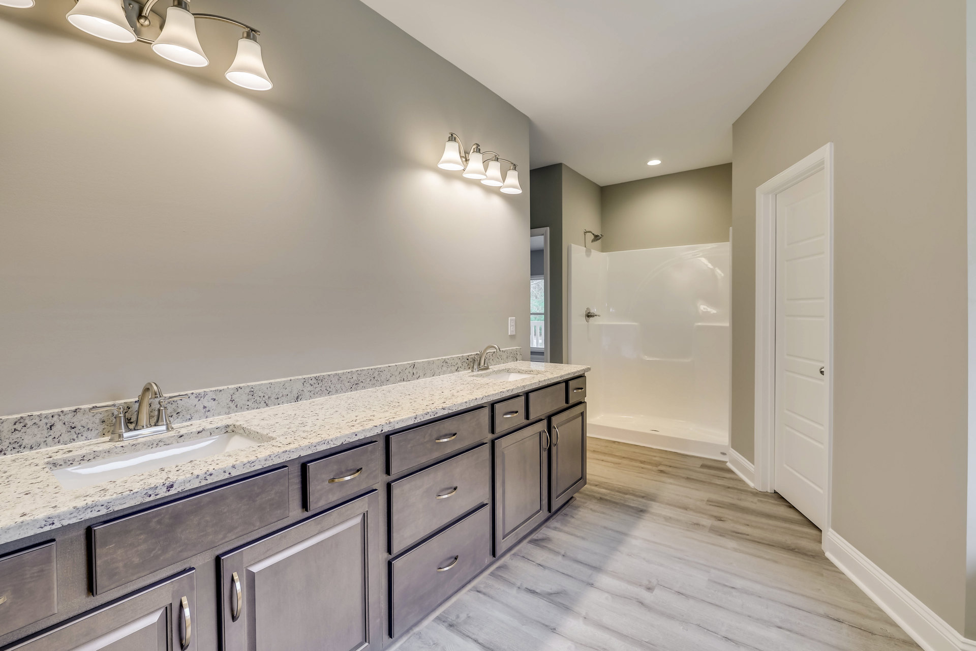 Bathroom with marble countertop, white sink, glass-enclosed shower, tile walls, and modern light fixture with four lamps and white shades