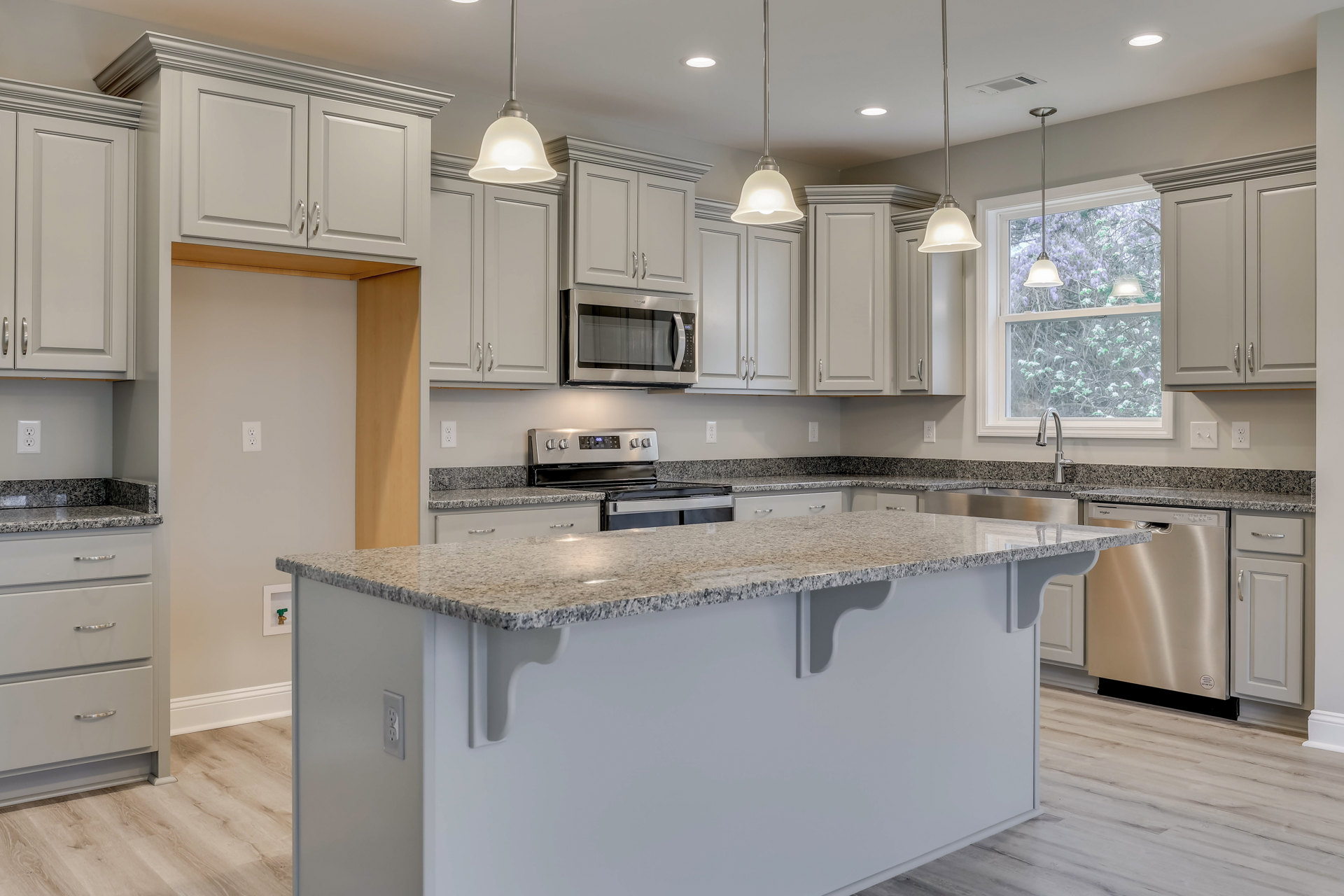 Granite kitchen island with built-in stove, white cabinetry with silver handles, stainless steel dishwasher, microwave, and white door with black handle
