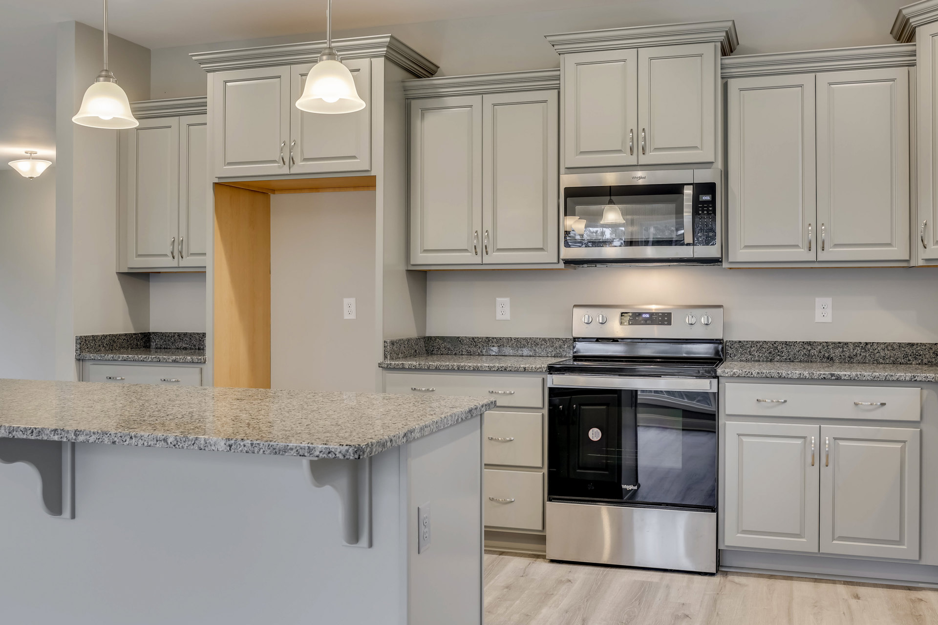 Granite countertops, wood cabinetry, stainless steel stove with glass door, built-in microwave, pendant light fixture, and neutral walls in a custom kitchen.