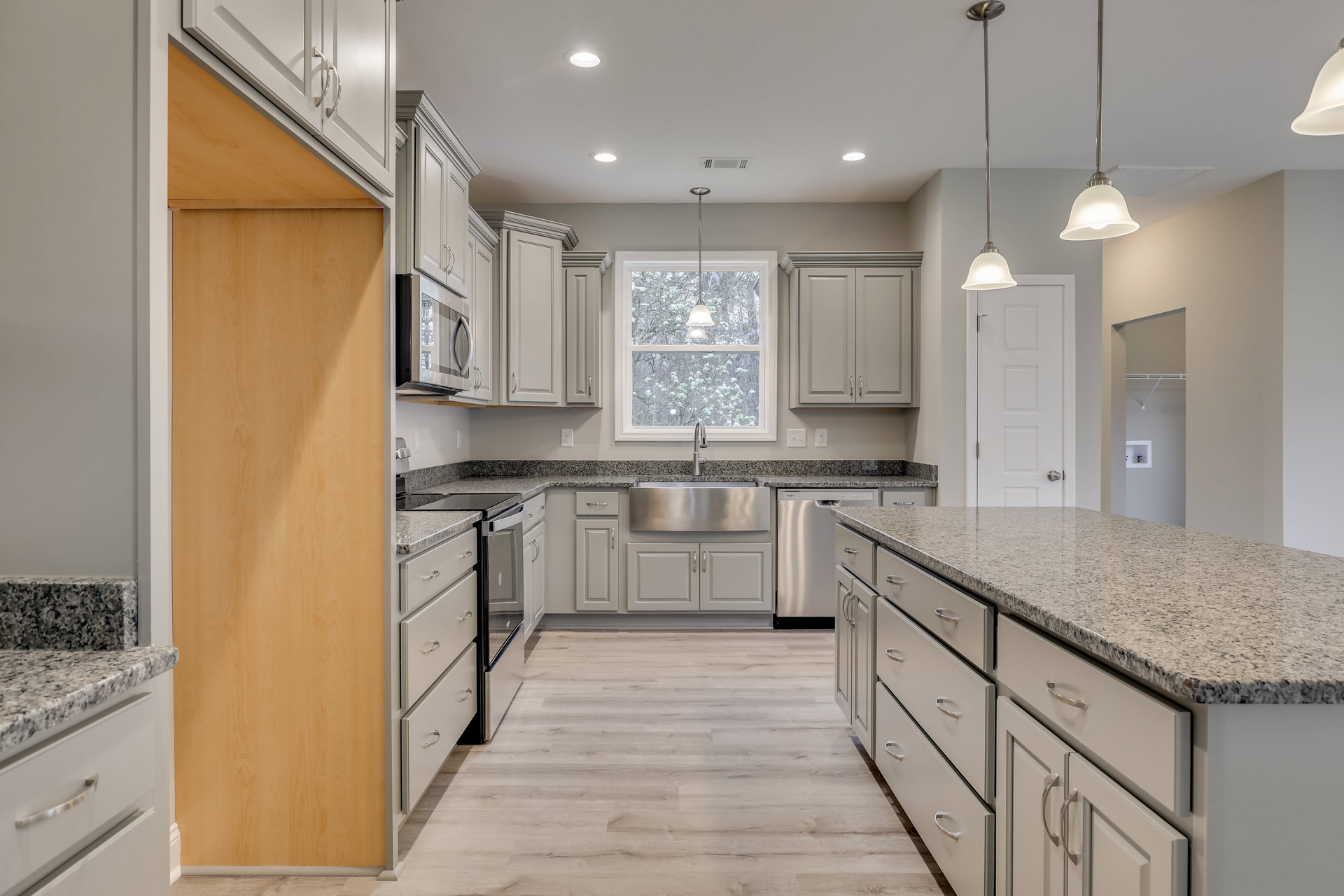 Granite countertops and stainless steel sink in a modern kitchen with white cabinets, silver handles, stainless steel dishwasher, marble counter, window, and overhead light fixture