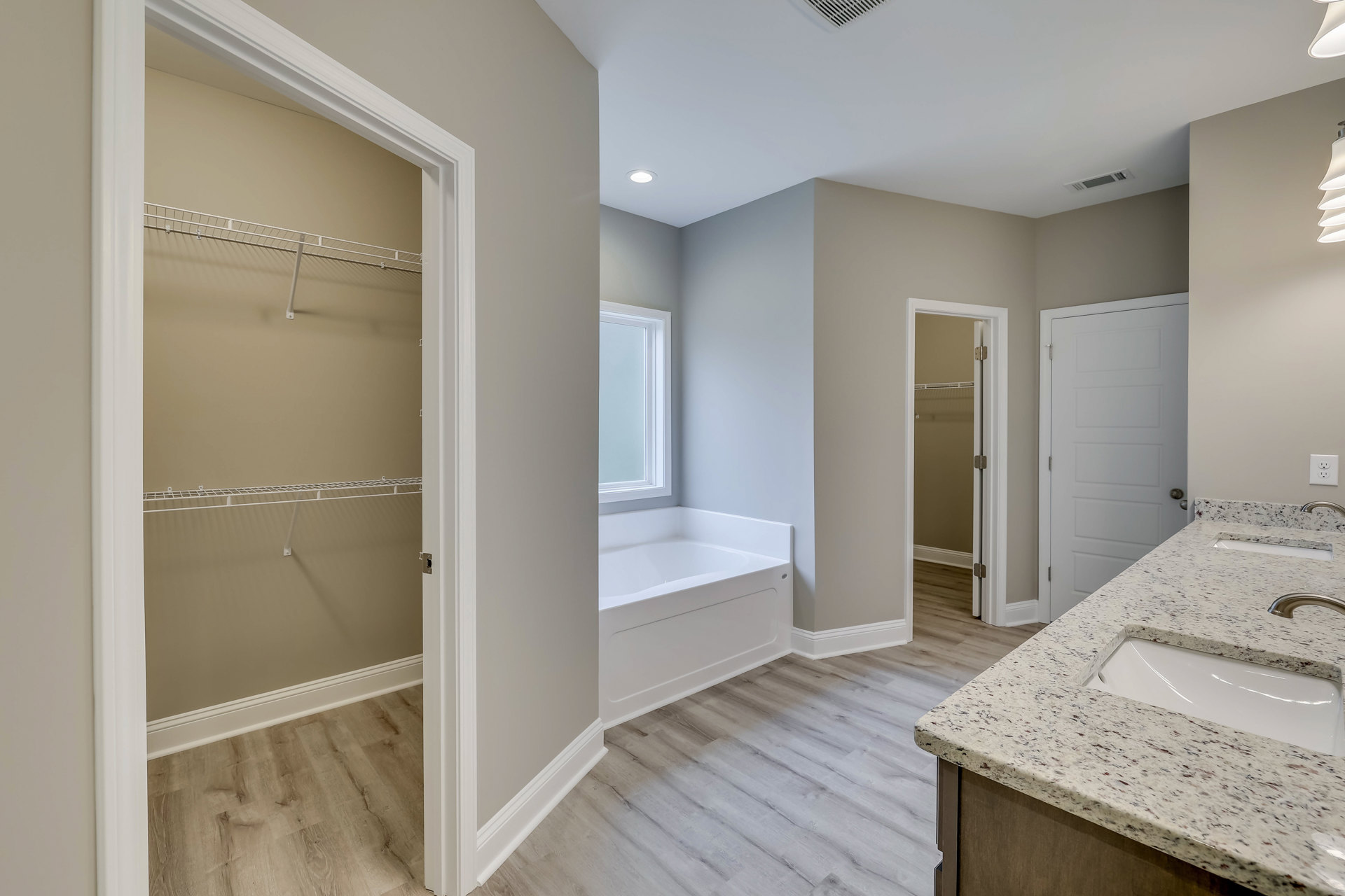 Bathroom with freestanding bathtub, marble countertop sink, white door with silver handle, and tile flooring; adjacent closet with white shelves visible.