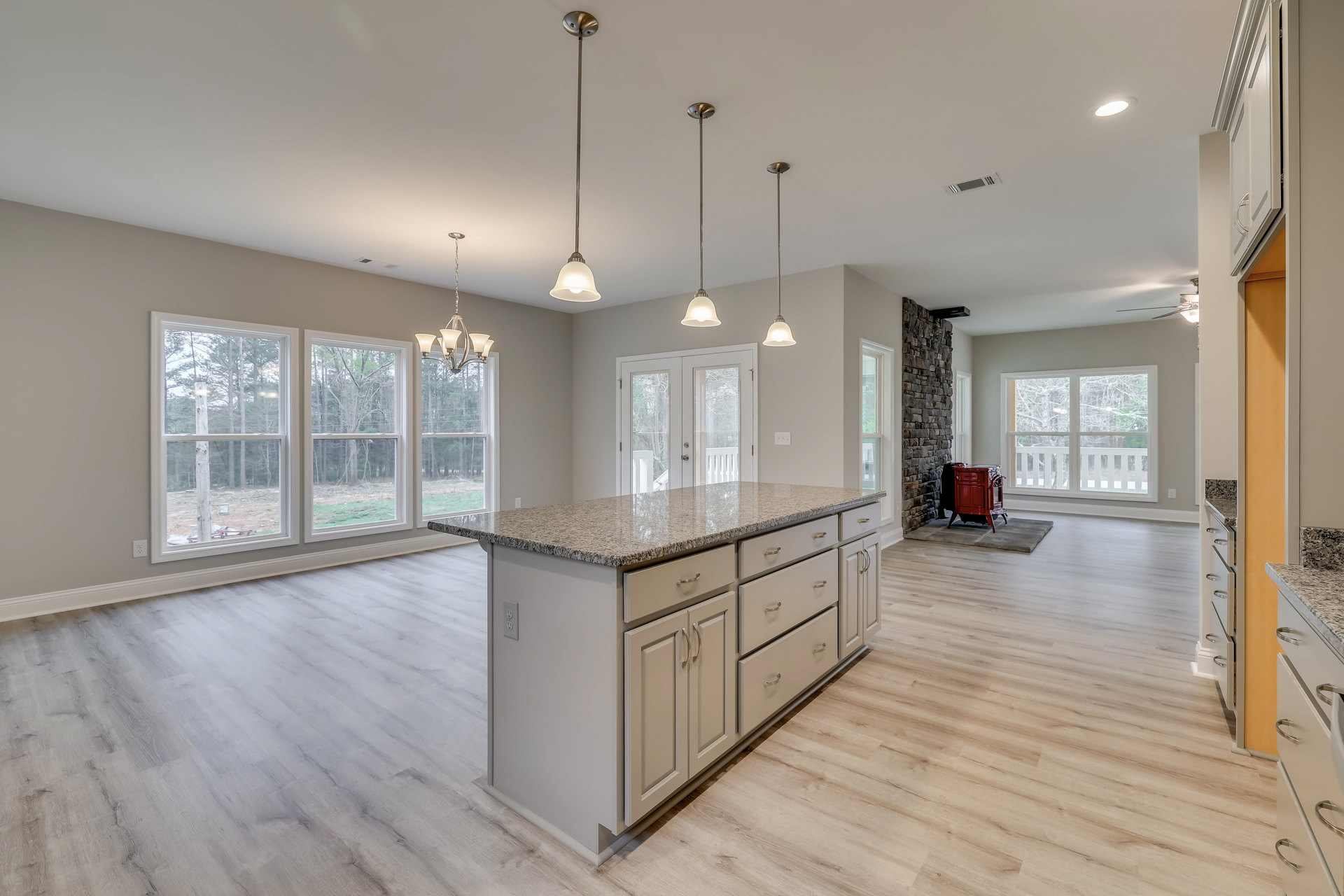 Open kitchen and dining area featuring a large central island with wood cabinetry, laminate countertops, wood flooring, a red wood stove set against a stone accent wall, modern