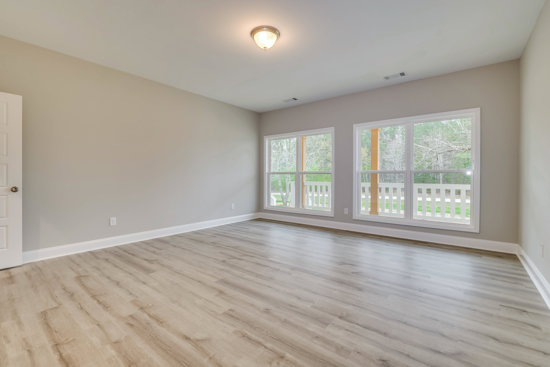 Room with hardwood flooring, large windows, white plaster walls, and ceiling light fixture