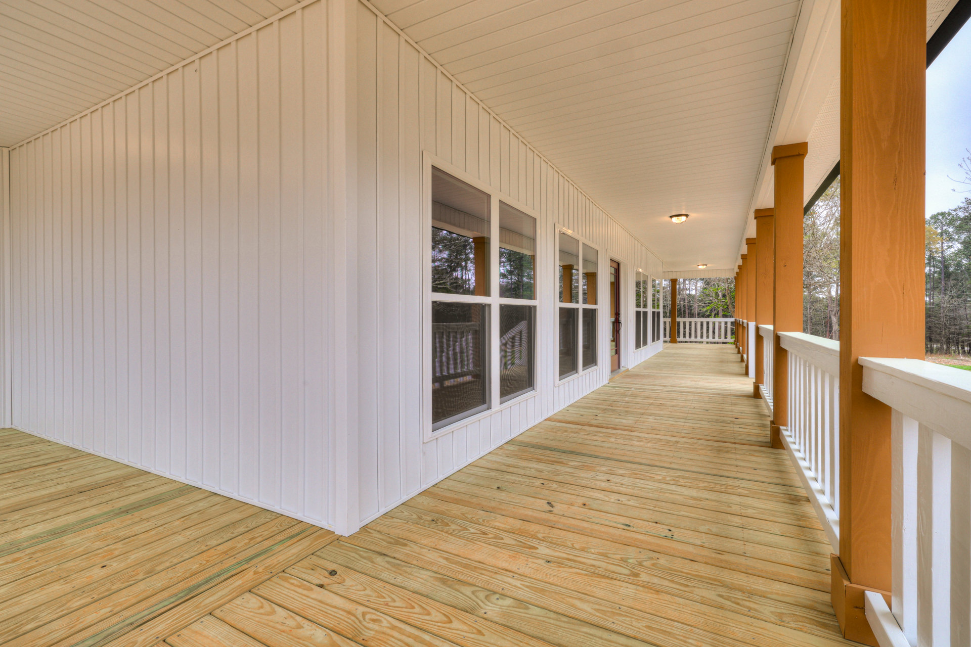 White exterior home with large windows and a spacious wood deck, featuring white trim and natural wood flooring