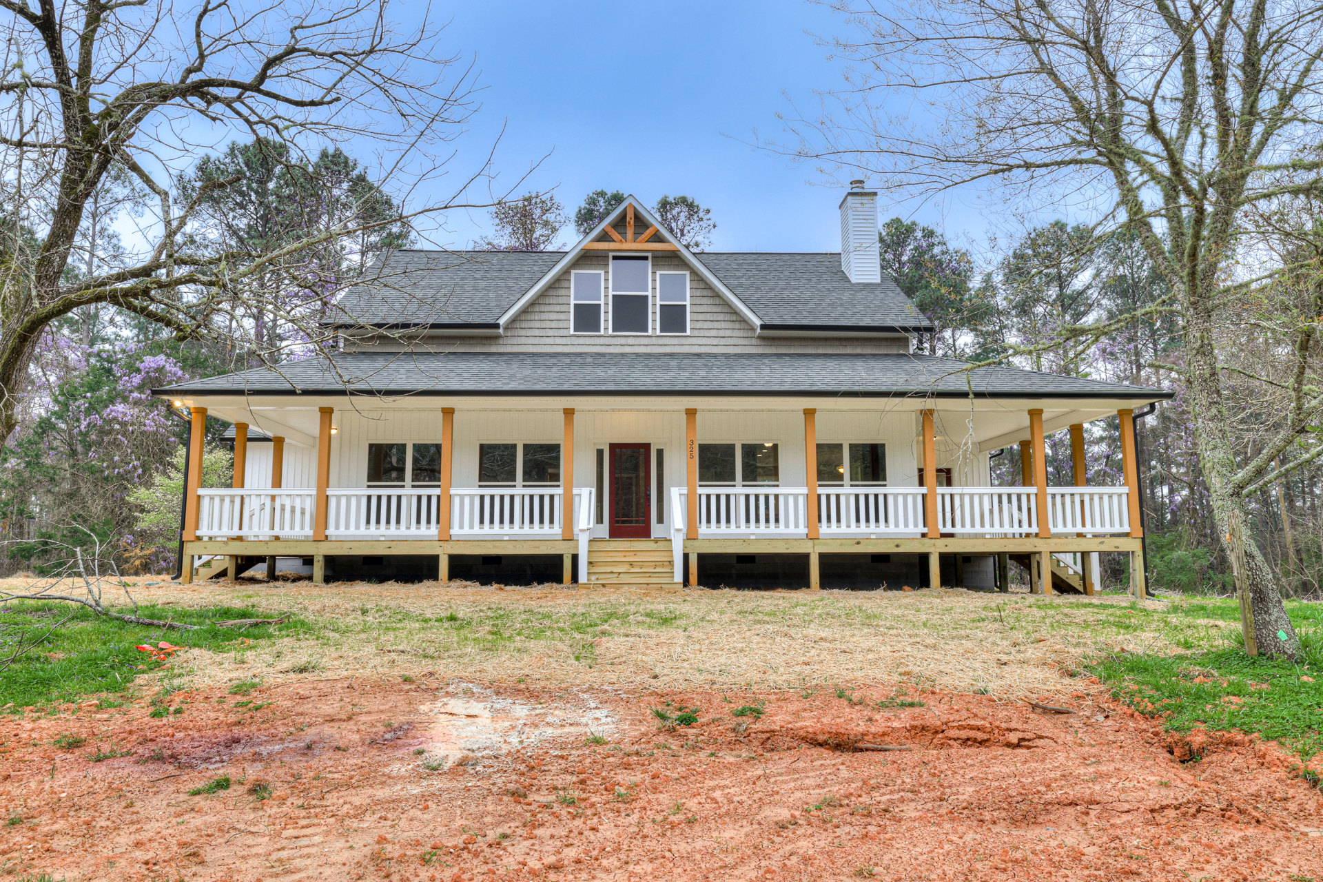 Two-story house with white siding, red front door, covered porch, square windows, grassy yard, and mature tree