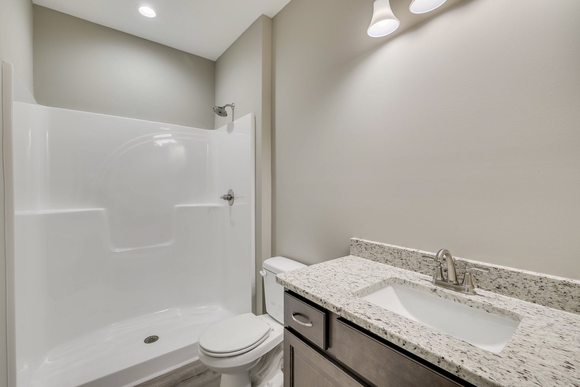 White tile bathroom with modern vanity, chrome faucet, rectangular sink, wall-mounted toilet, glass shower enclosure, and neutral stone countertop