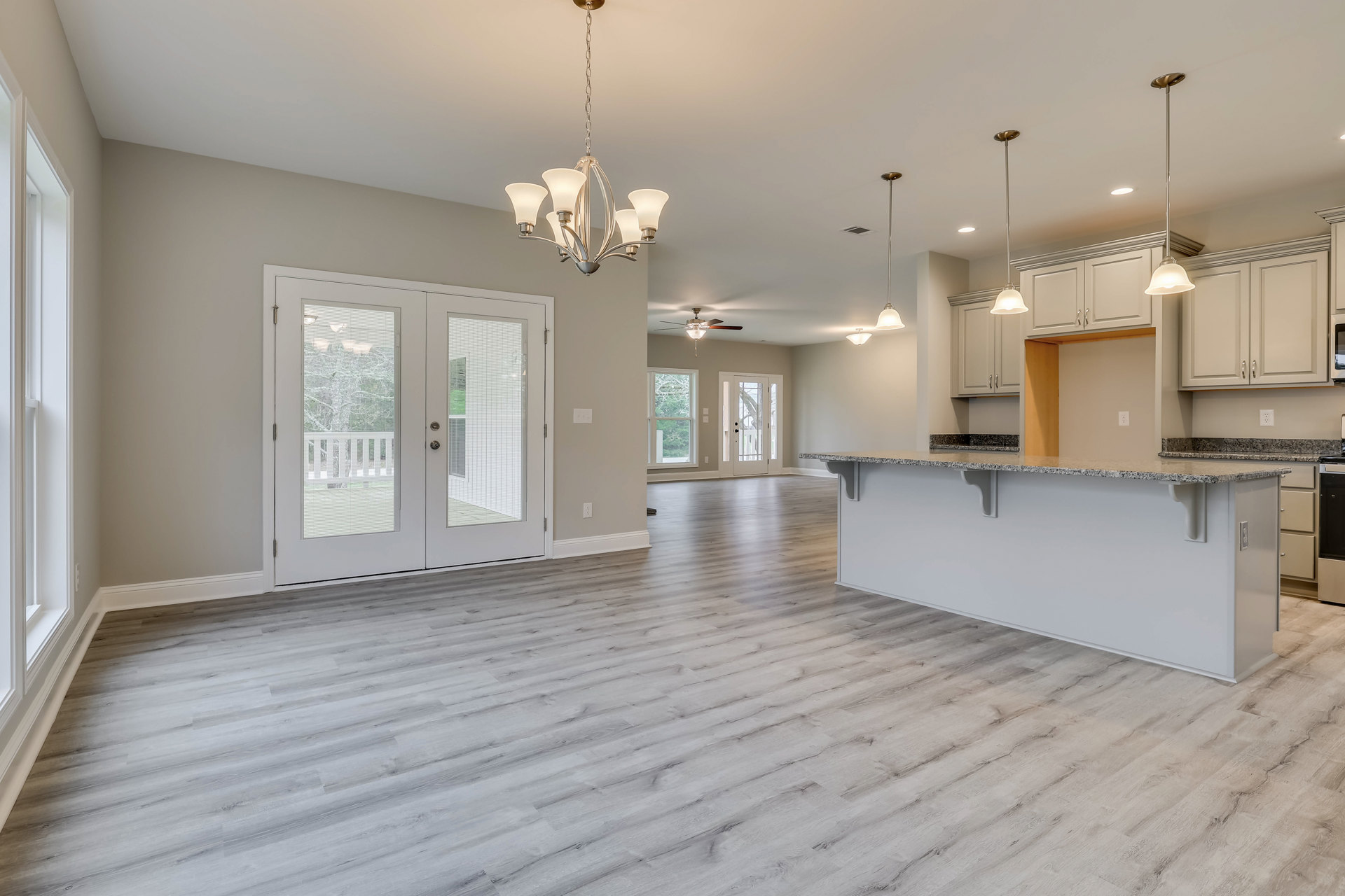Open kitchen and dining area with wood flooring, white cabinetry, bar counter, glass-paneled double doors, five-light chandelier, and white door with blinds
