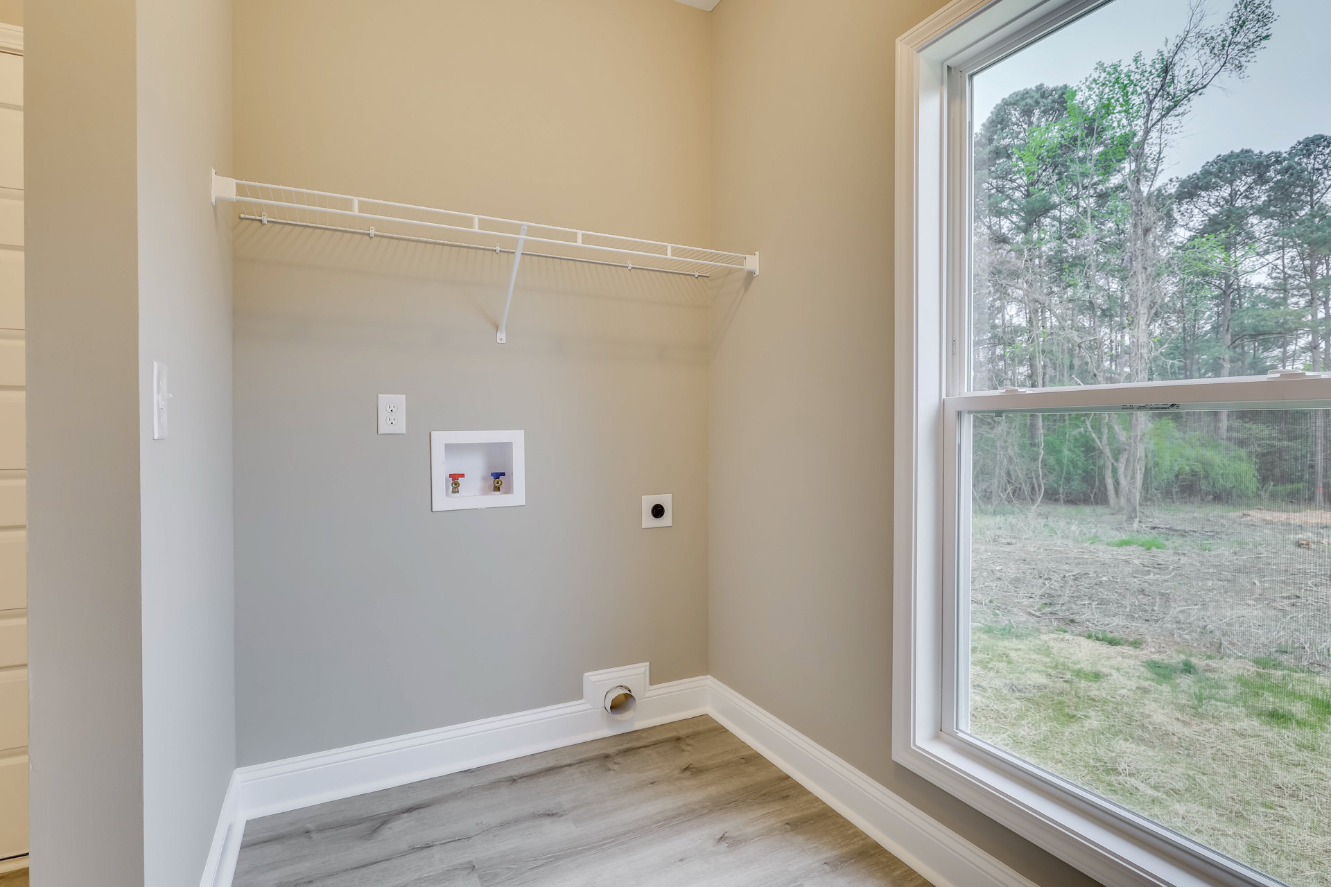 Bathroom with wood flooring, white walls, closet featuring a shelf and toilet, window screened with trees visible outside, white utility box with two valves mounted on wall.