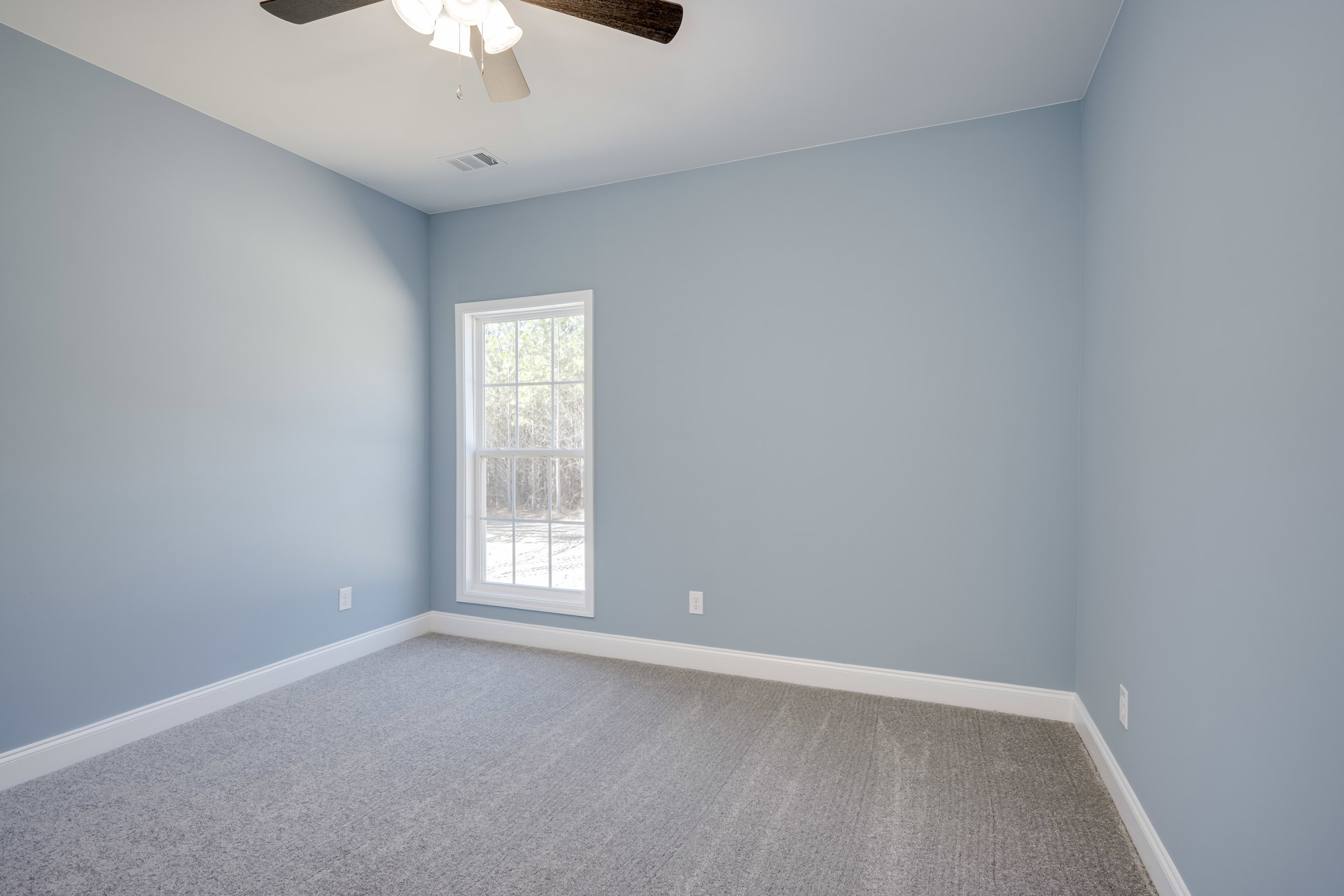 Carpeted bedroom with white walls, ceiling fan with light fixture, large window overlooking trees, and decorative crown molding