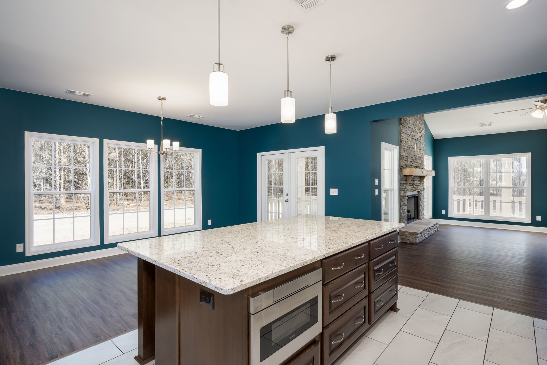 Spacious kitchen featuring a large central island with built-in microwave, stainless steel oven with glass door, white cabinetry, tile backsplash, and windows with white trim