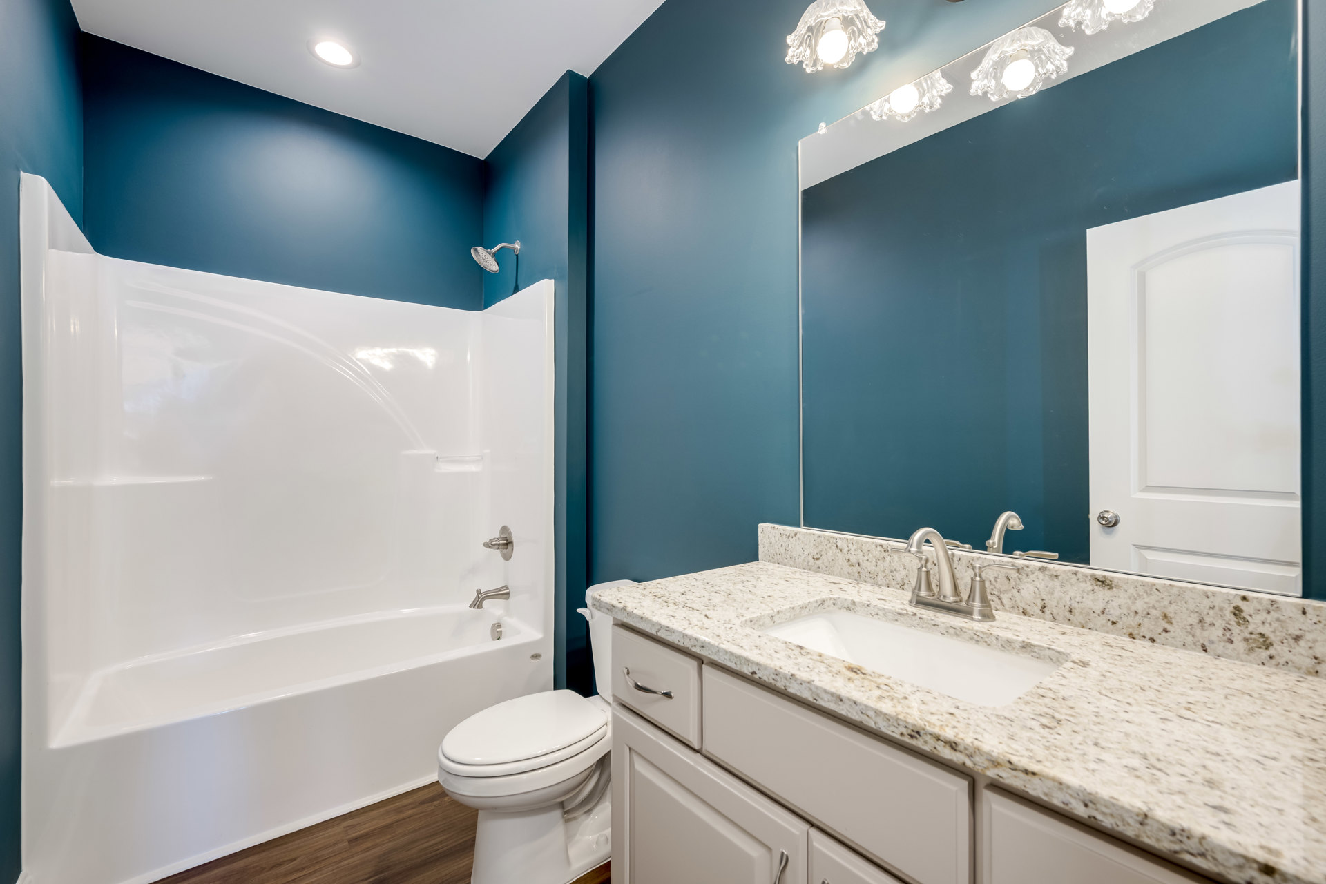 White bathtub and sink with chrome fixtures, blue accent wall, white toilet, tile flooring, white cabinetry, and closed door in a modern bathroom.