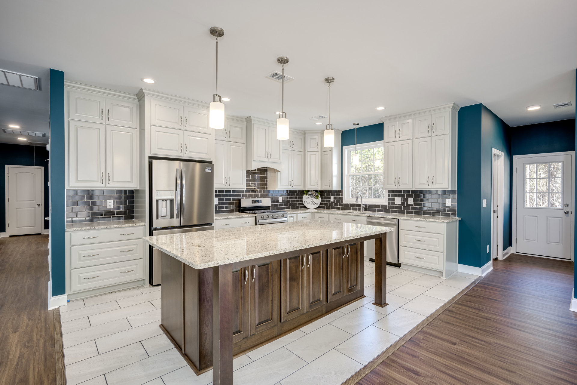 Kitchen with white cabinets, marble island countertop, stainless steel refrigerator with ice and water dispenser, tile flooring, glass-paneled white door, and decorative sign with