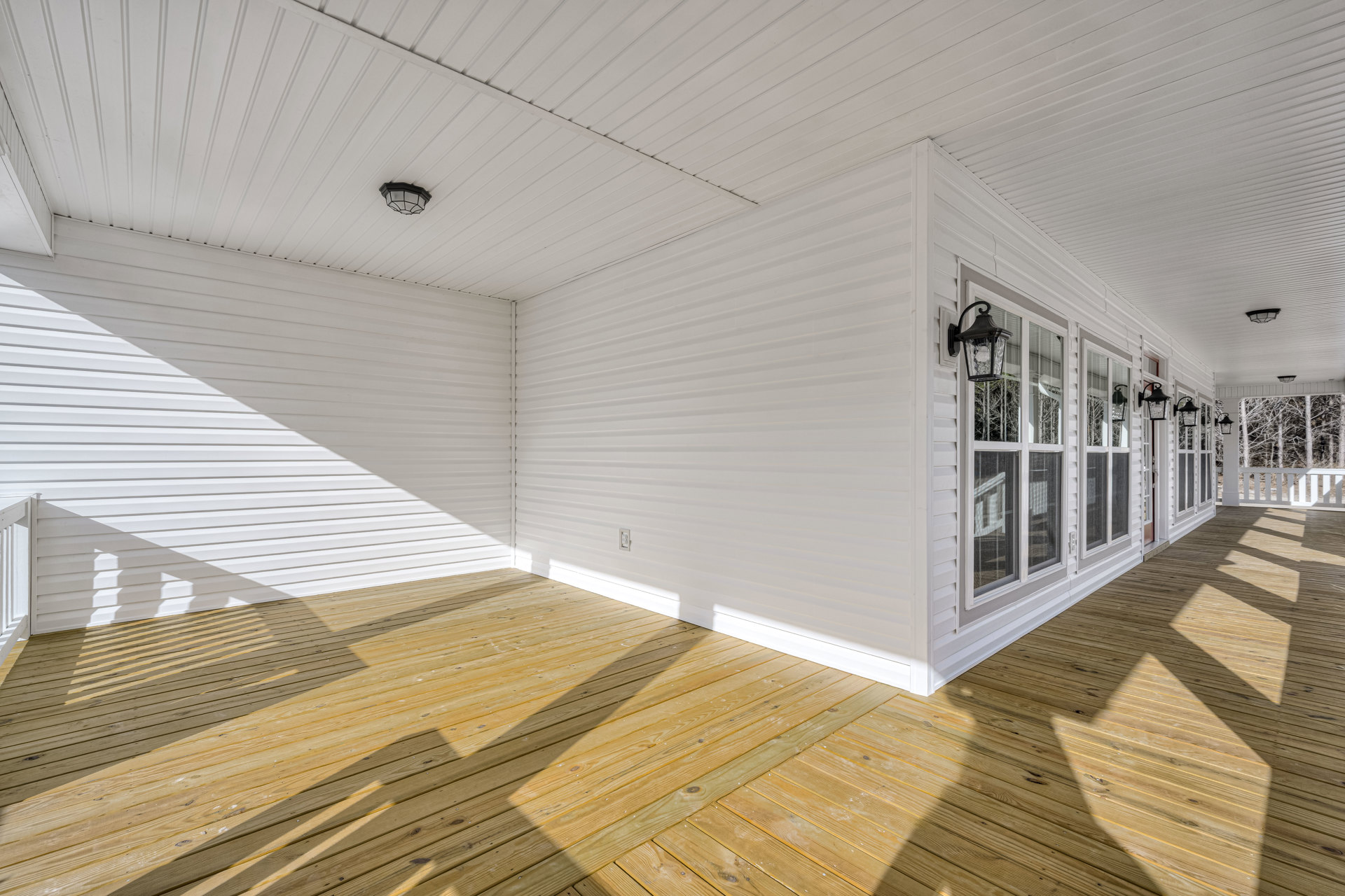 White exterior with horizontal wood deck, white walls, linear ceiling panels, large windows, and modern light fixture.