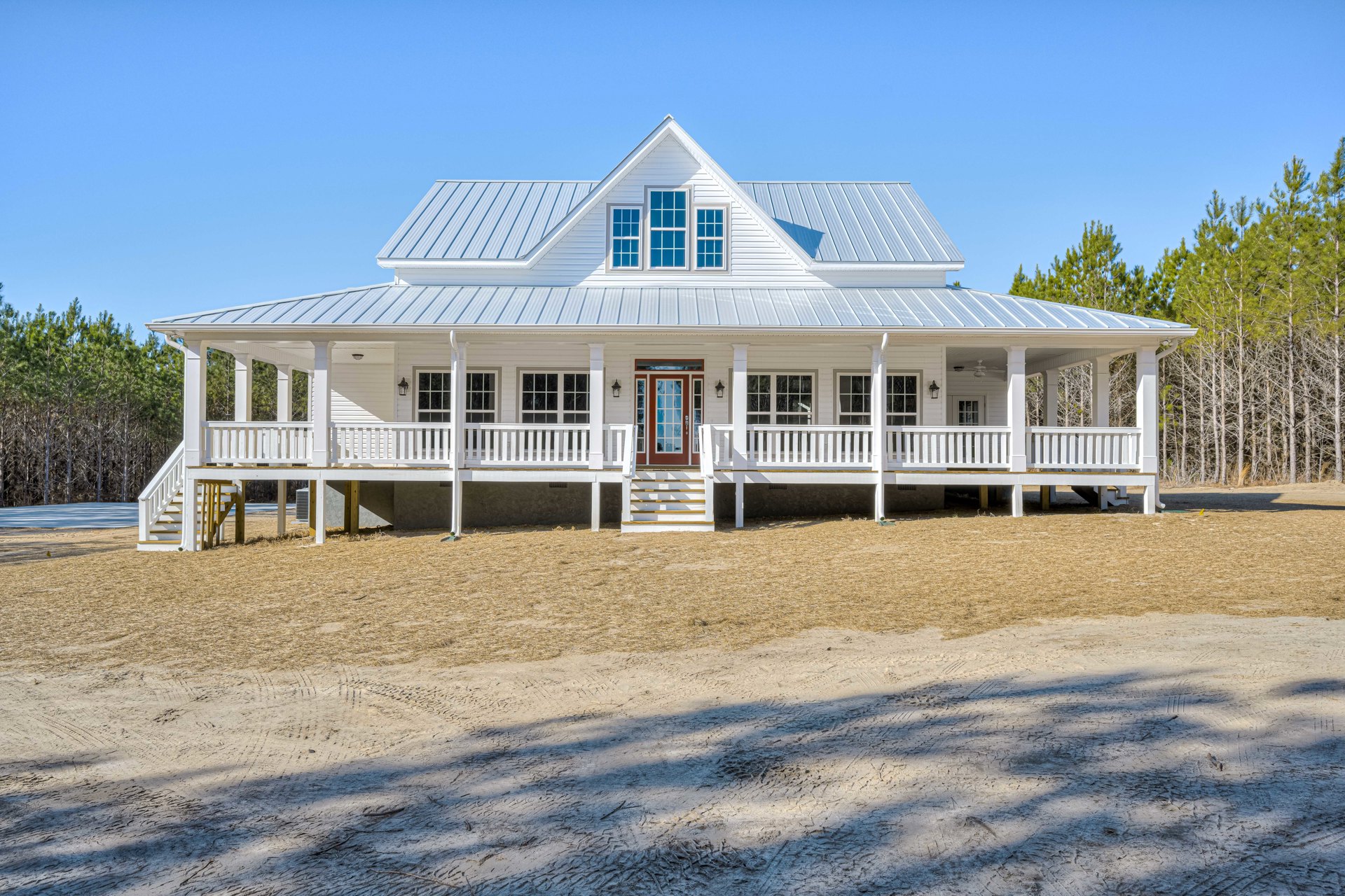 White siding house with covered porch, red front door, gabled roof, multiple windows, and landscaped front yard.