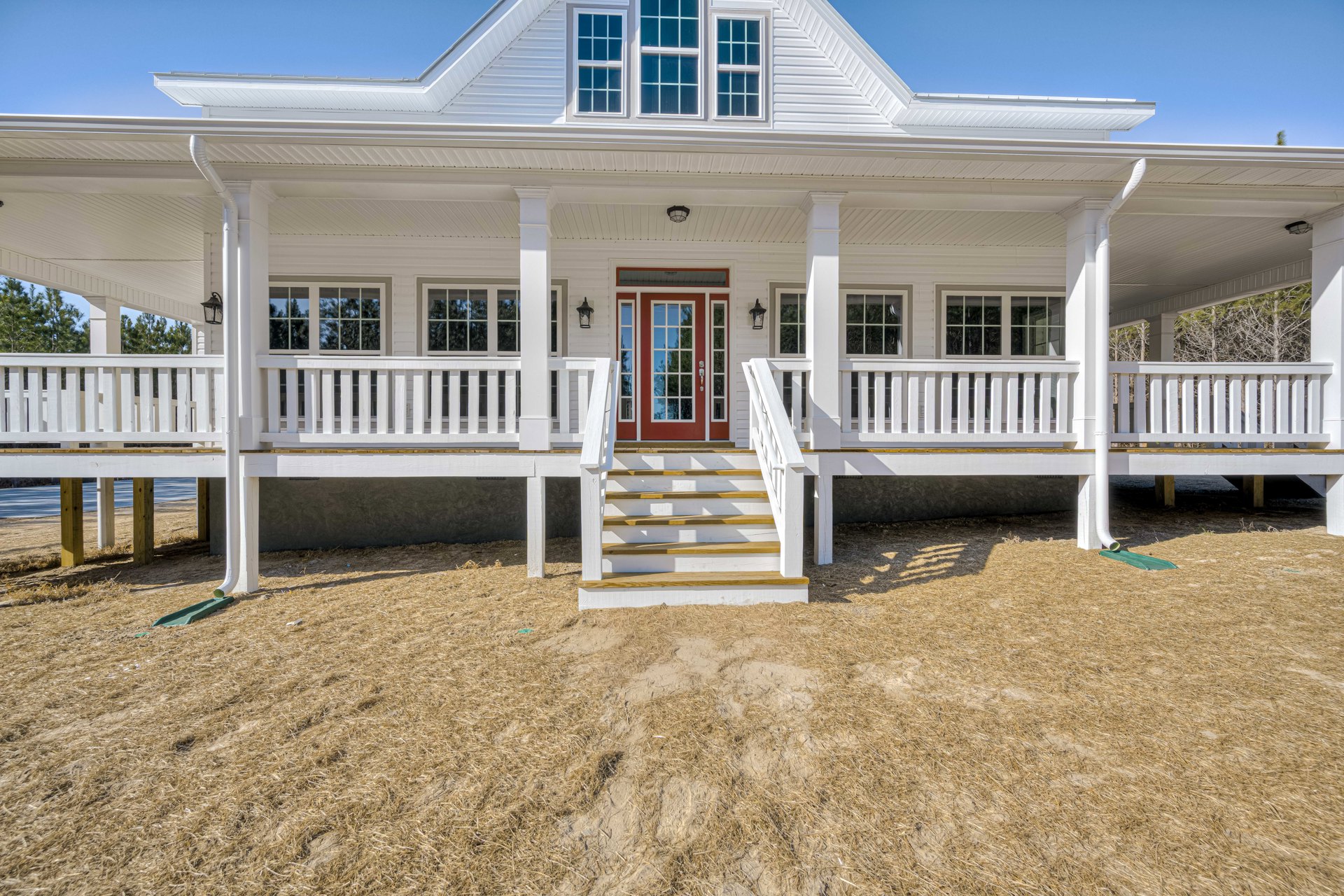 White siding exterior with a red front door, glass window panels, white-framed windows, and white stairs leading up from a dirt yard.