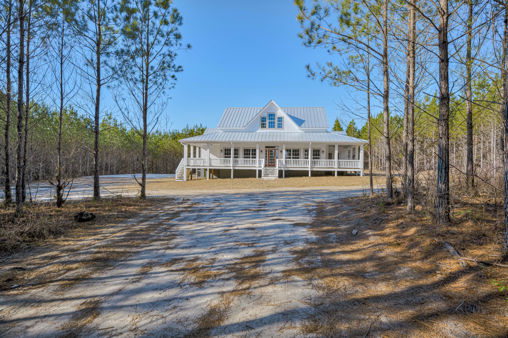 White siding house with red front door, covered porch, surrounded by tall trees, snow-covered lawn with tree shadows.