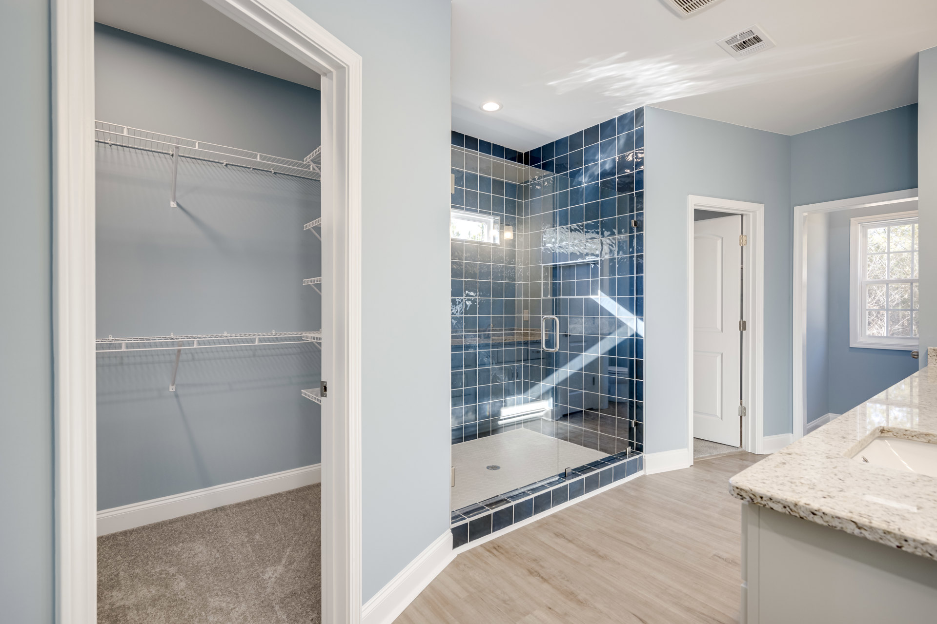 Bathroom with glass walk-in shower, tiled walls and floor, single sink vanity, window overlooking trees, white shelving in adjacent closet, hinged door visible