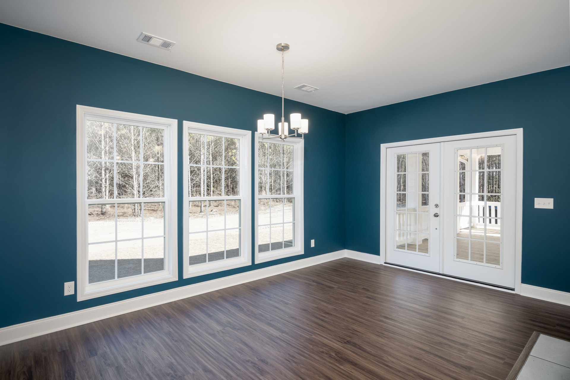 Wood flooring and white double doors with glass panes, large windows overlooking trees, chandelier hanging from plaster ceiling