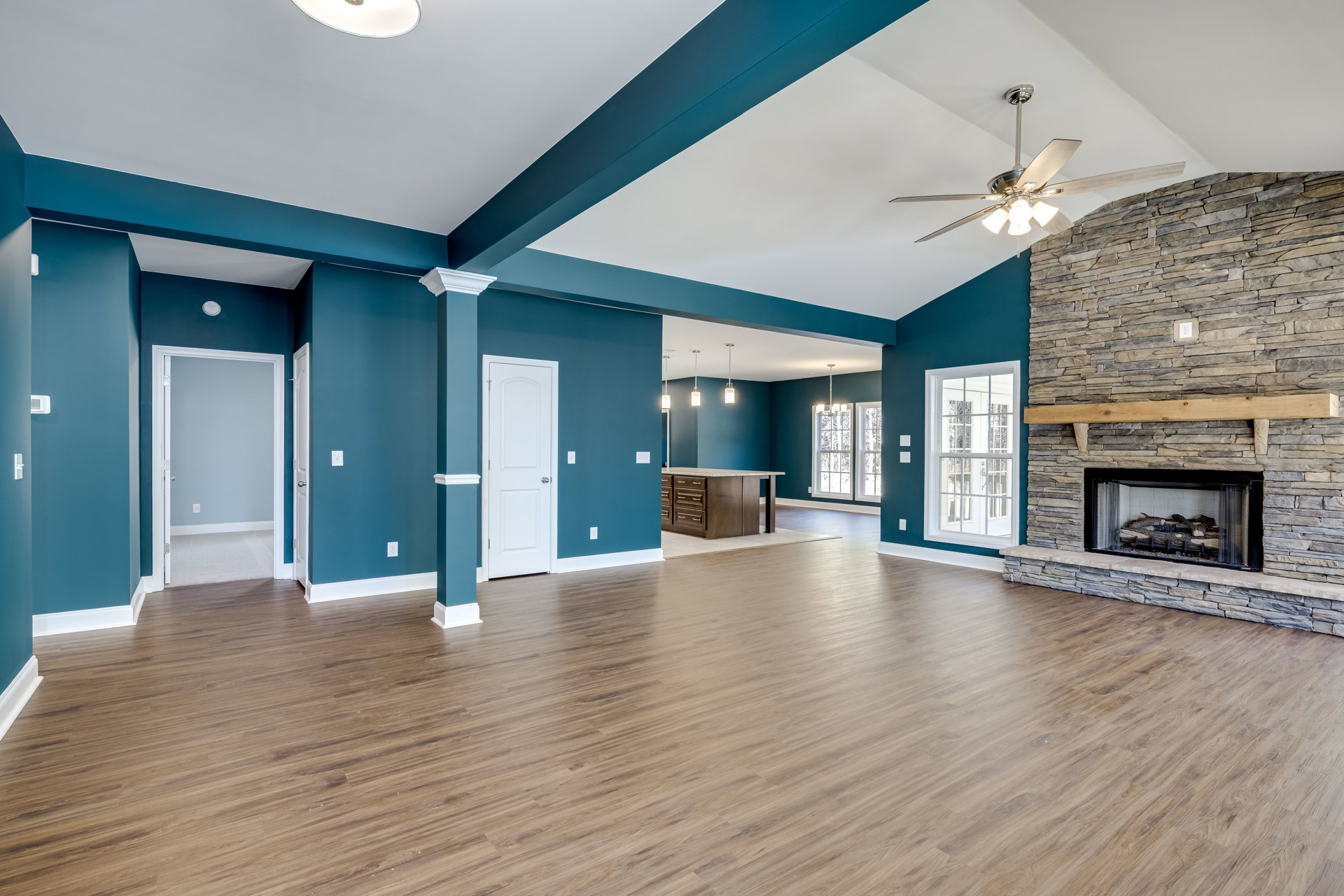 Spacious living room featuring wood flooring, blue accent wall, fireplace with stacked logs, large window, and white door with silver handle