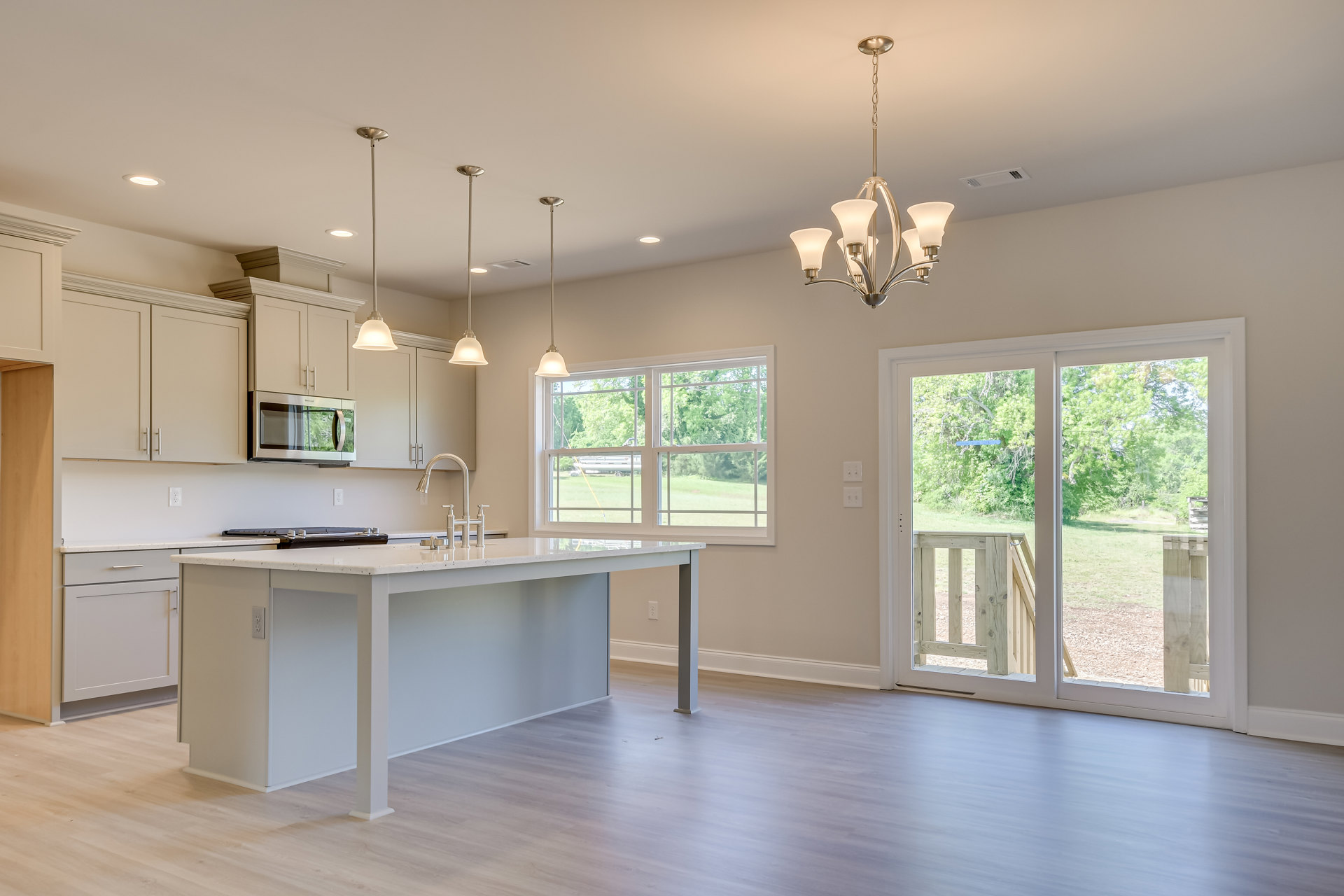 White kitchen island with quartz countertop, wood flooring, shaker cabinetry, stainless steel microwave, sliding glass door opening to backyard, dining table, modern chandelier