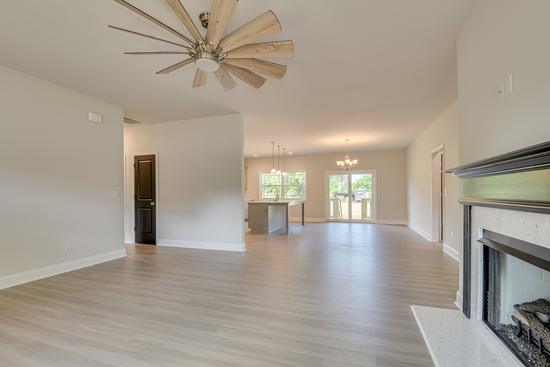 Open-concept living area featuring hardwood floors, white kitchen island with pendant lighting, ceiling fan, glass door leading to backyard, and neutral walls with crown molding