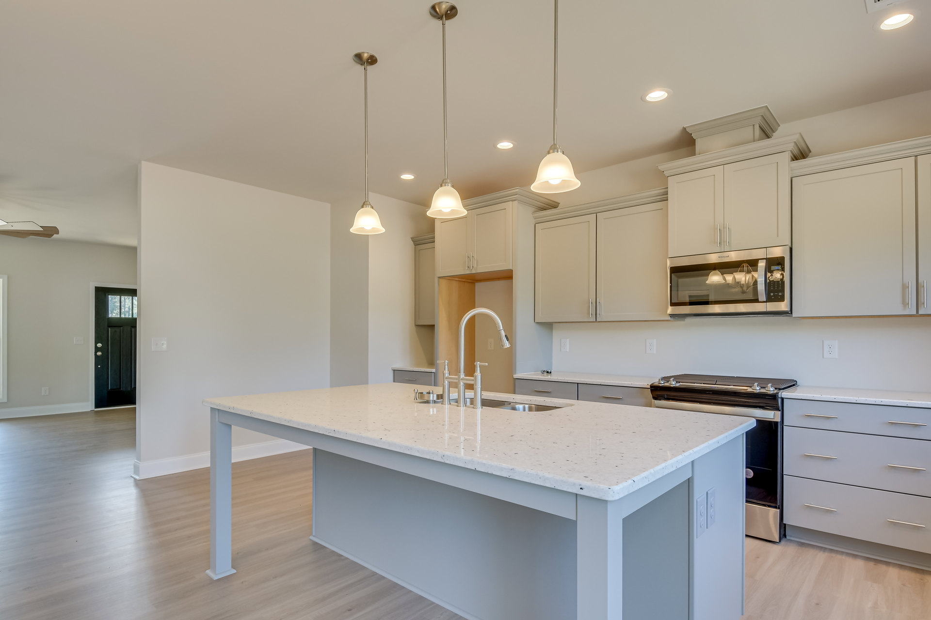Spacious kitchen featuring a large white island with built-in sink, white cabinetry with silver handles, tiled backsplash, stainless steel appliances, and pendant lighting above