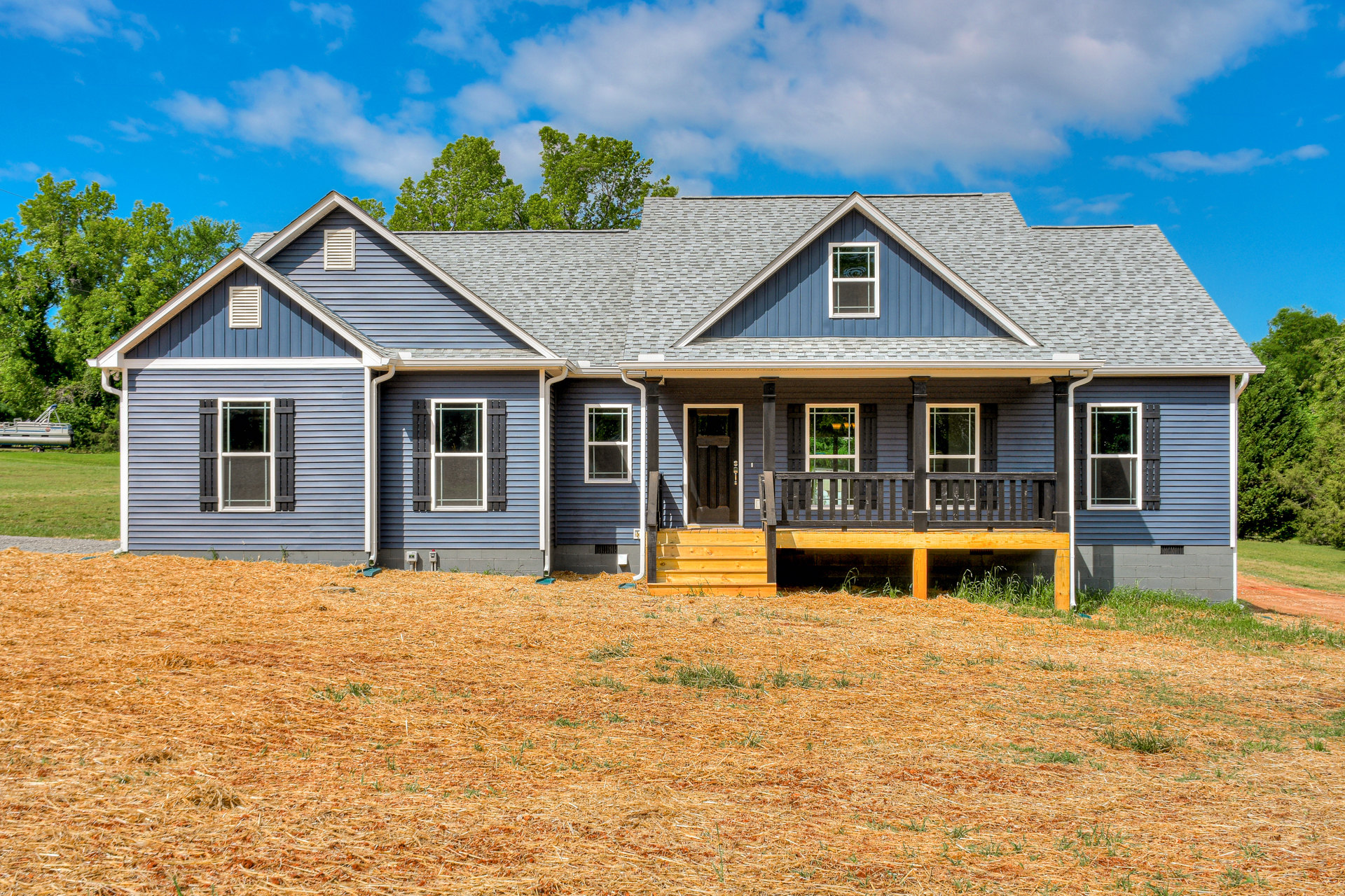 Two-story home with white-framed windows, covered front porch, and expansive green lawn bordered by a wooden fence; mature tree reflected in window glass.