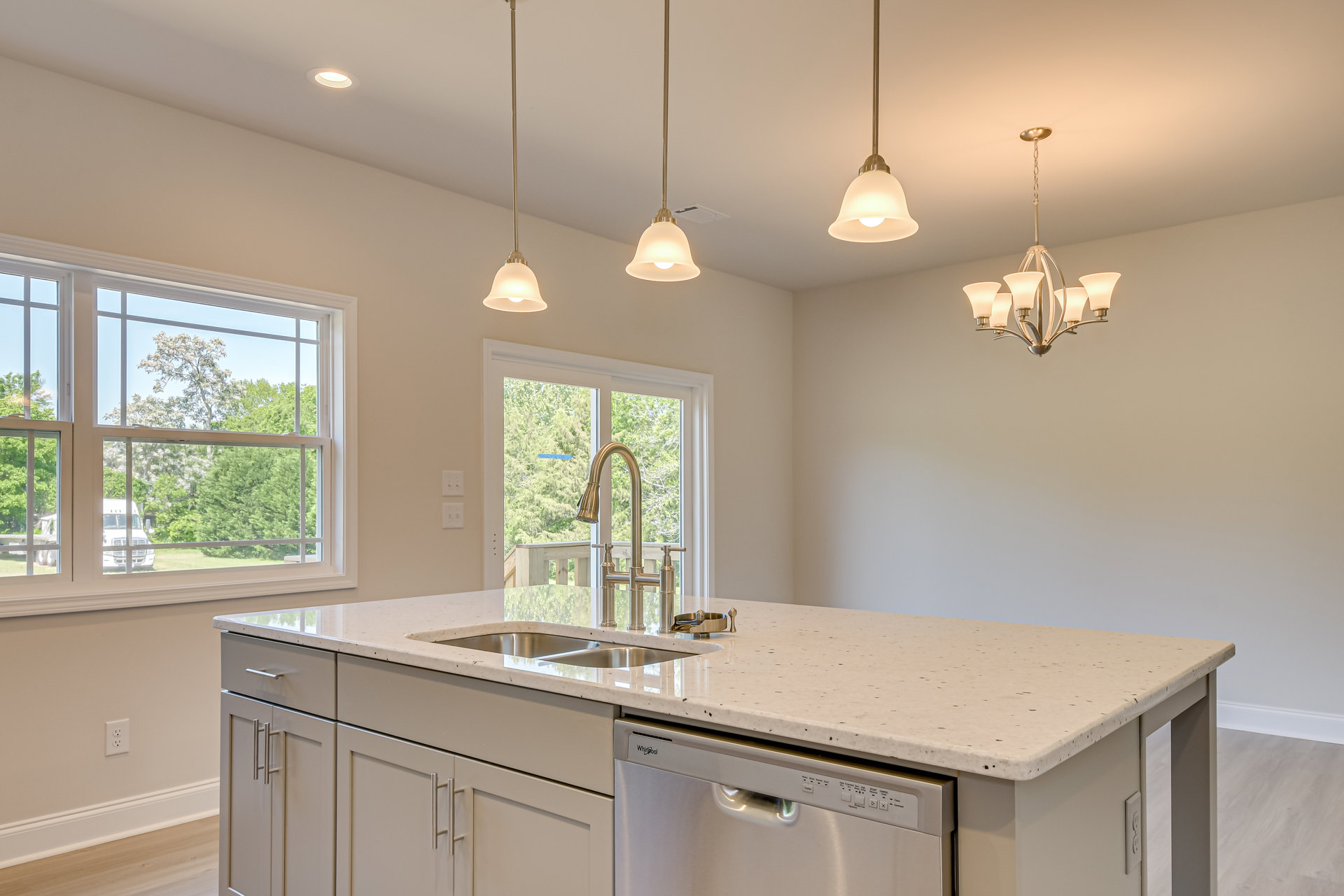 White kitchen cabinetry with brushed nickel hardware, stainless steel dishwasher beneath quartz countertop, undermount sink with chrome faucet, large window overlooking green