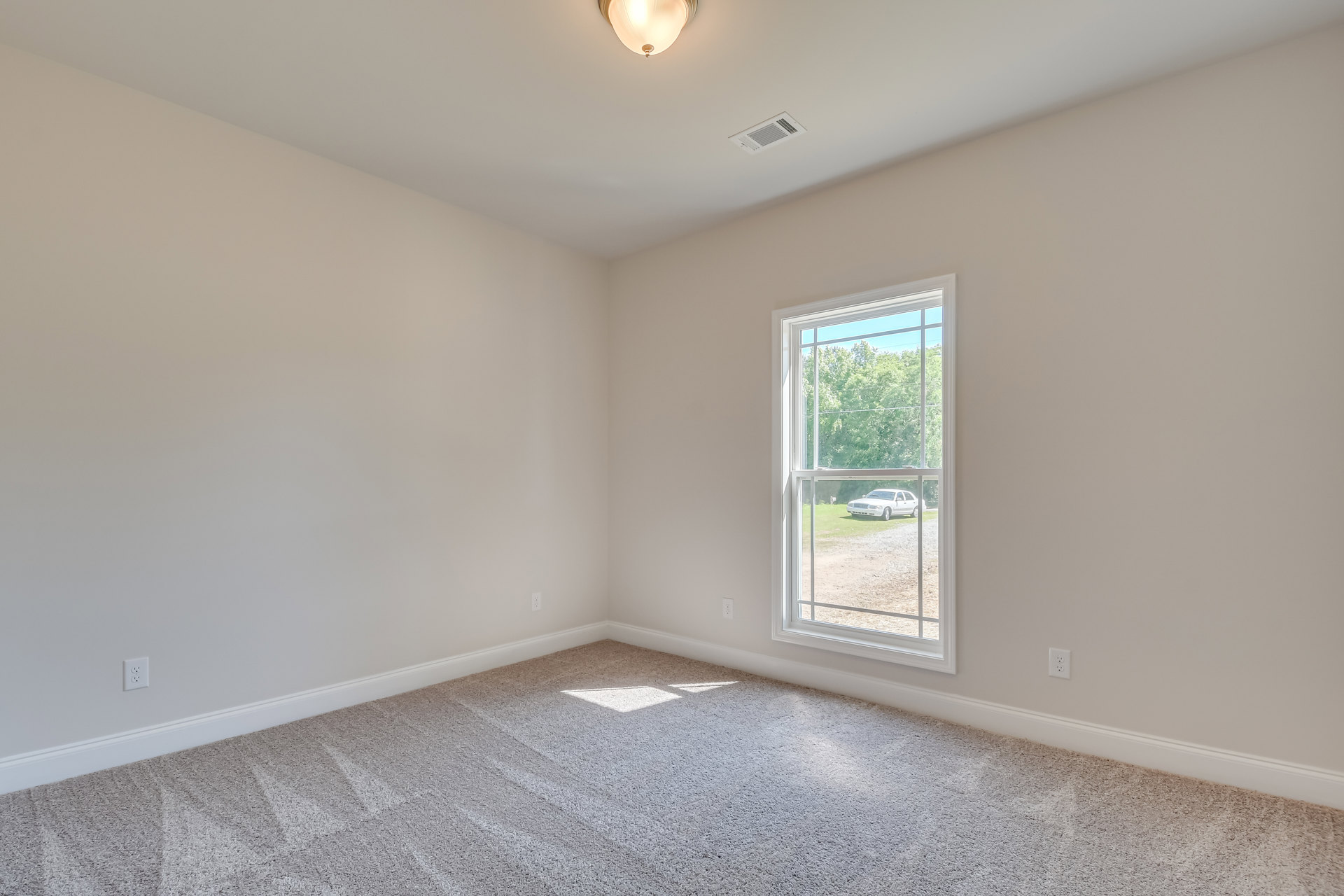 Carpeted bedroom with white walls, large window overlooking driveway, ceiling vent, and modern light fixture