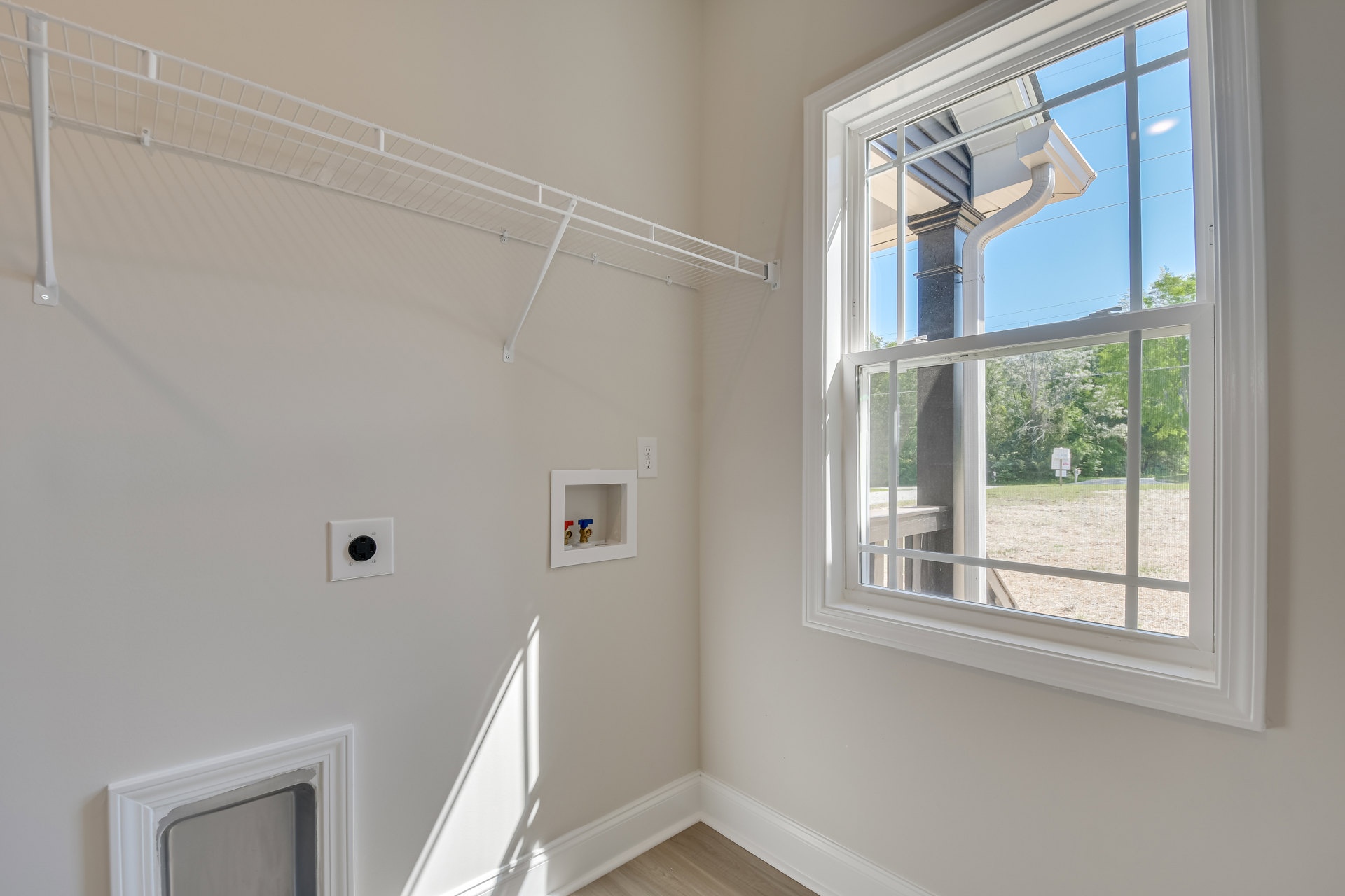 Bright room with white walls, window with white trim, built-in shelf, wall outlet, and crown molding; view of neighboring house and gutter through window.