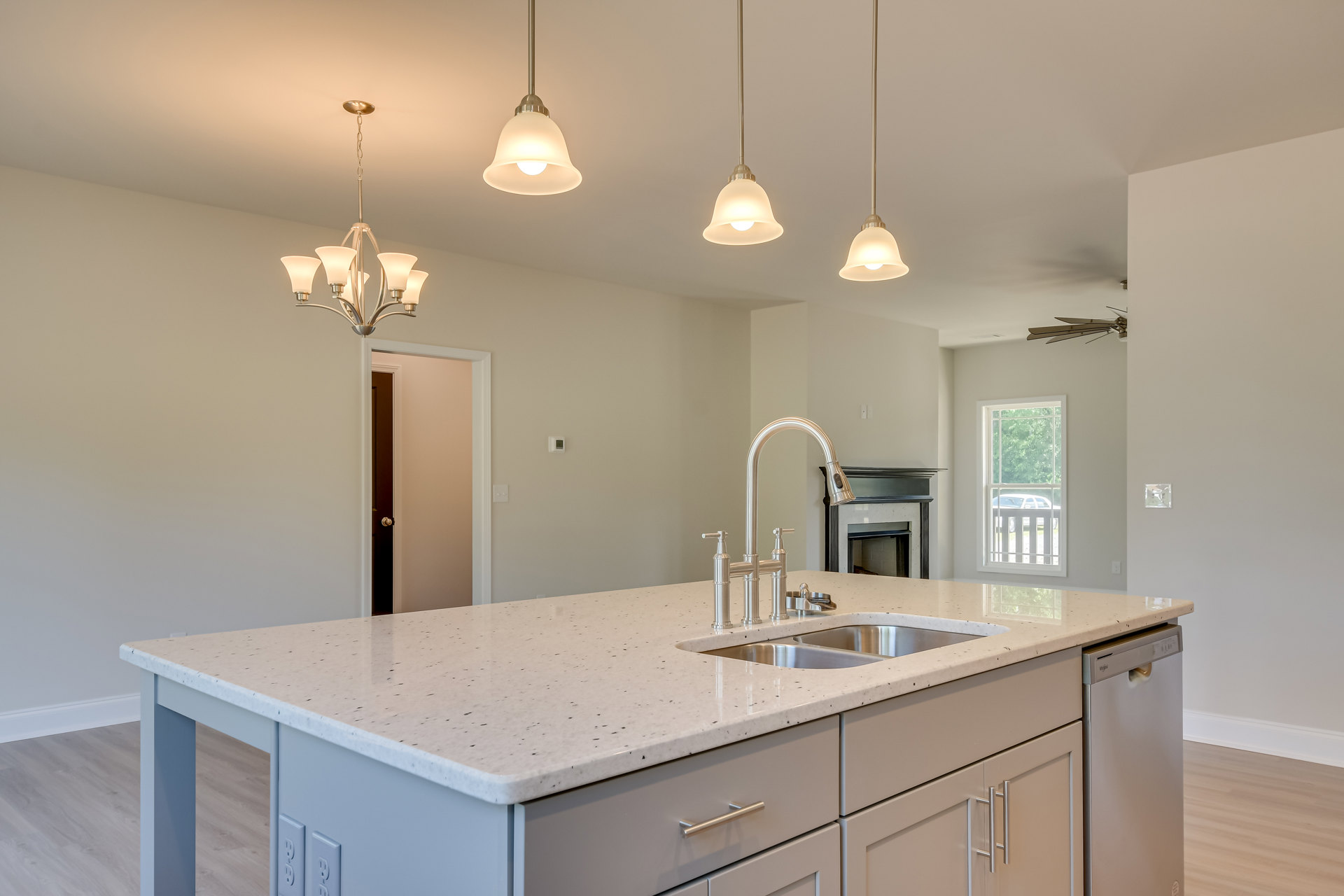 Kitchen island with two sinks and faucets, light-colored countertop, modern cabinetry, stainless steel appliances, pendant light fixtures, window with partial outdoor view