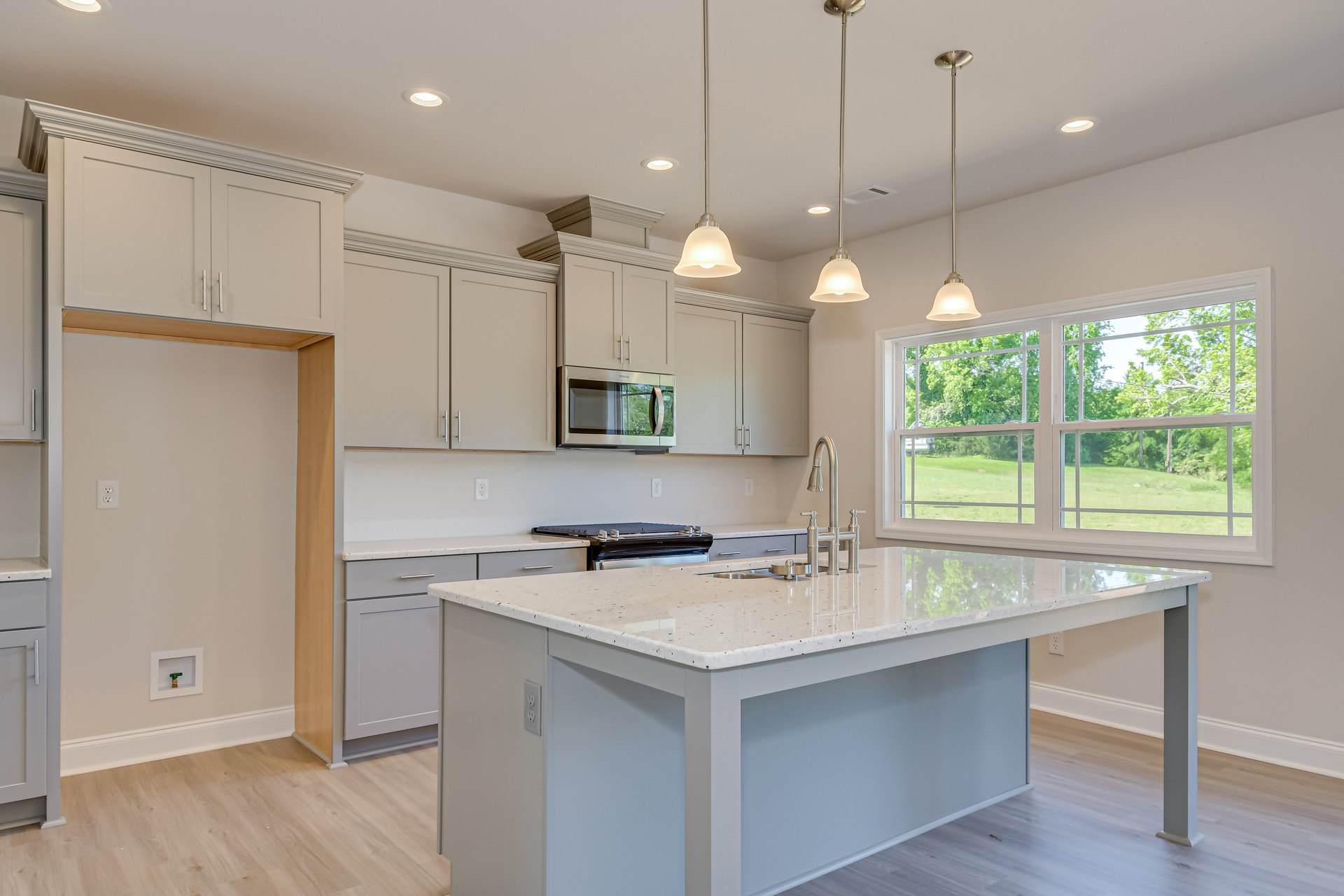 Spacious kitchen featuring a large central island with built-in stove, white cabinetry, tile backsplash, open microwave door, and exposed metal pipe along the white ceiling