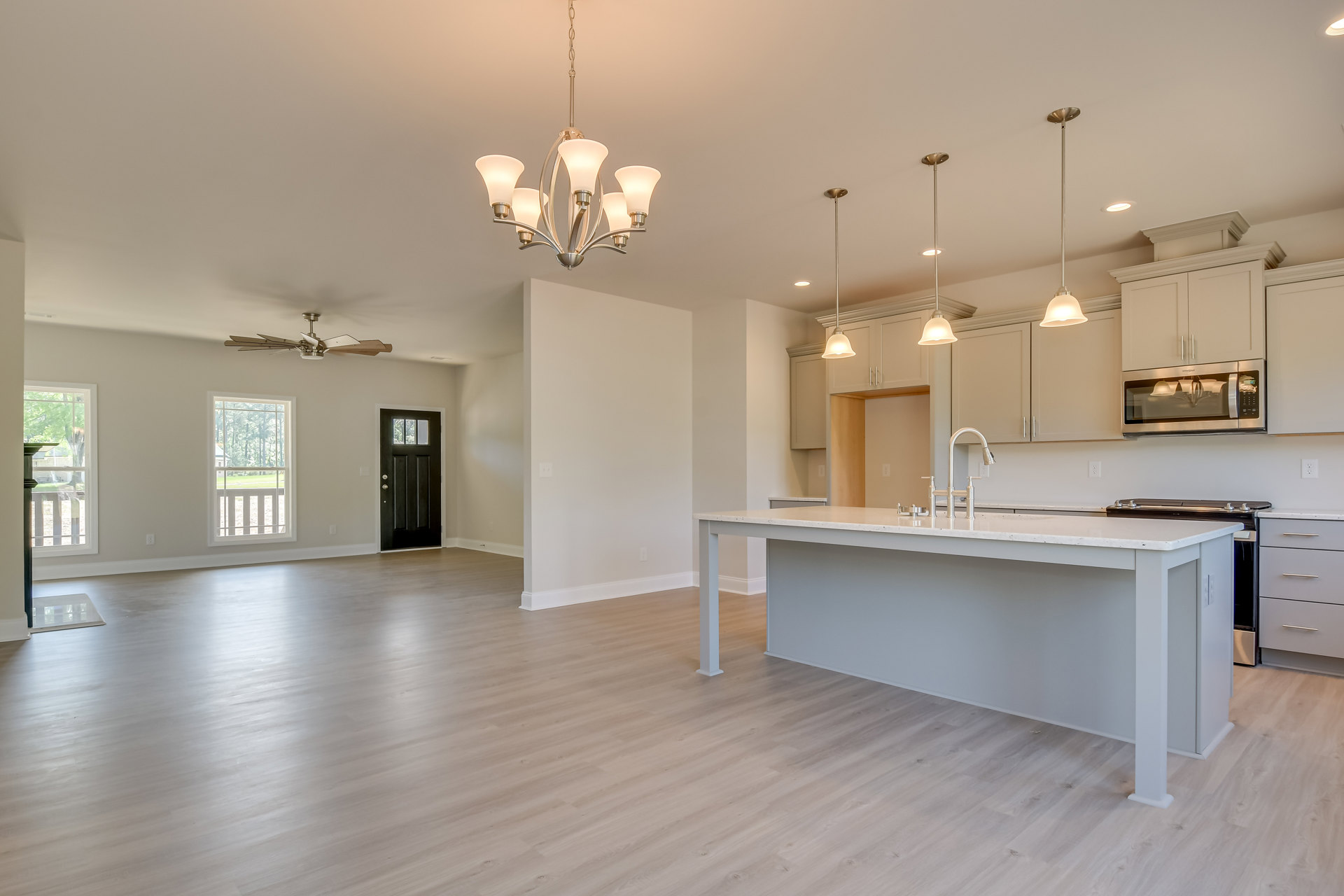 Open-concept kitchen and living room with wood laminate flooring, white cabinetry, stone countertops, stainless steel sink, and a five-light chandelier; large window with trees