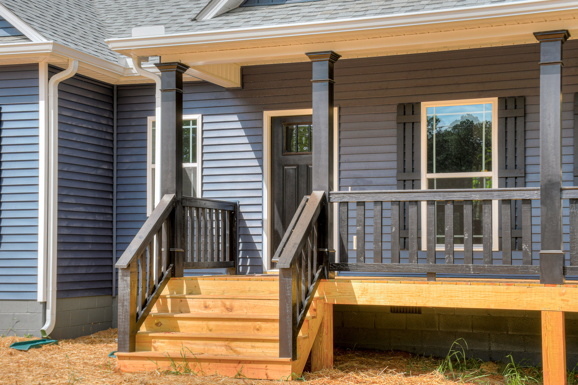 Wooden porch with stairs, white baluster and handrail, shingle roof with white gutter, exterior siding, window overlooking trees