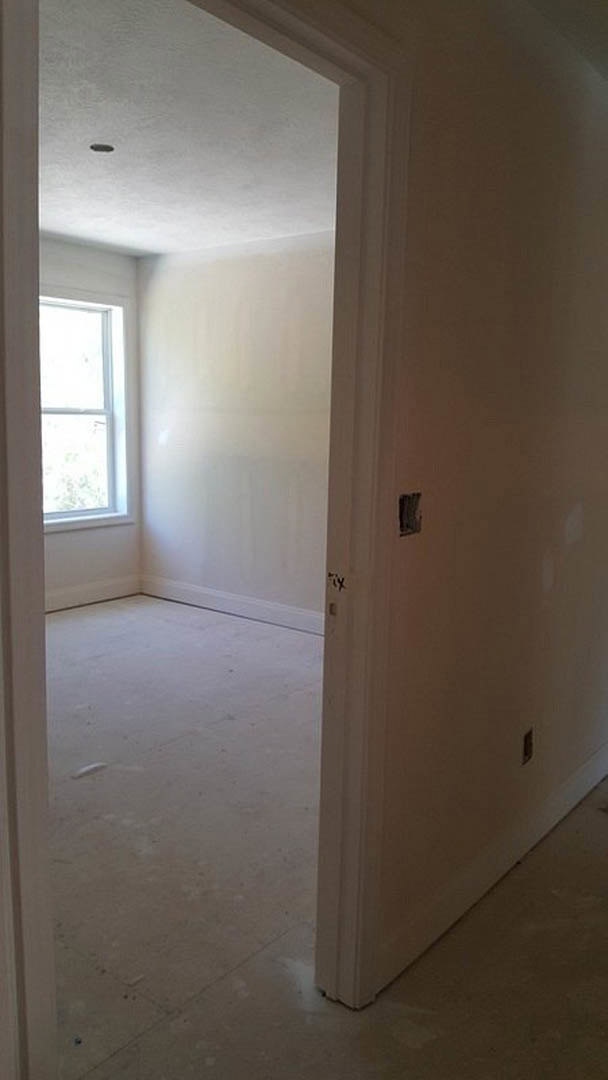Concrete floor and white plaster walls in a modern room, open door revealing adjacent space, white-framed window letting in natural light.