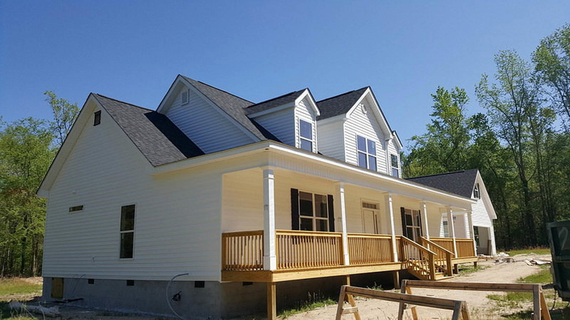 White siding house with covered porch, wooden railing, white-framed windows, black shutters, and landscaped front yard.