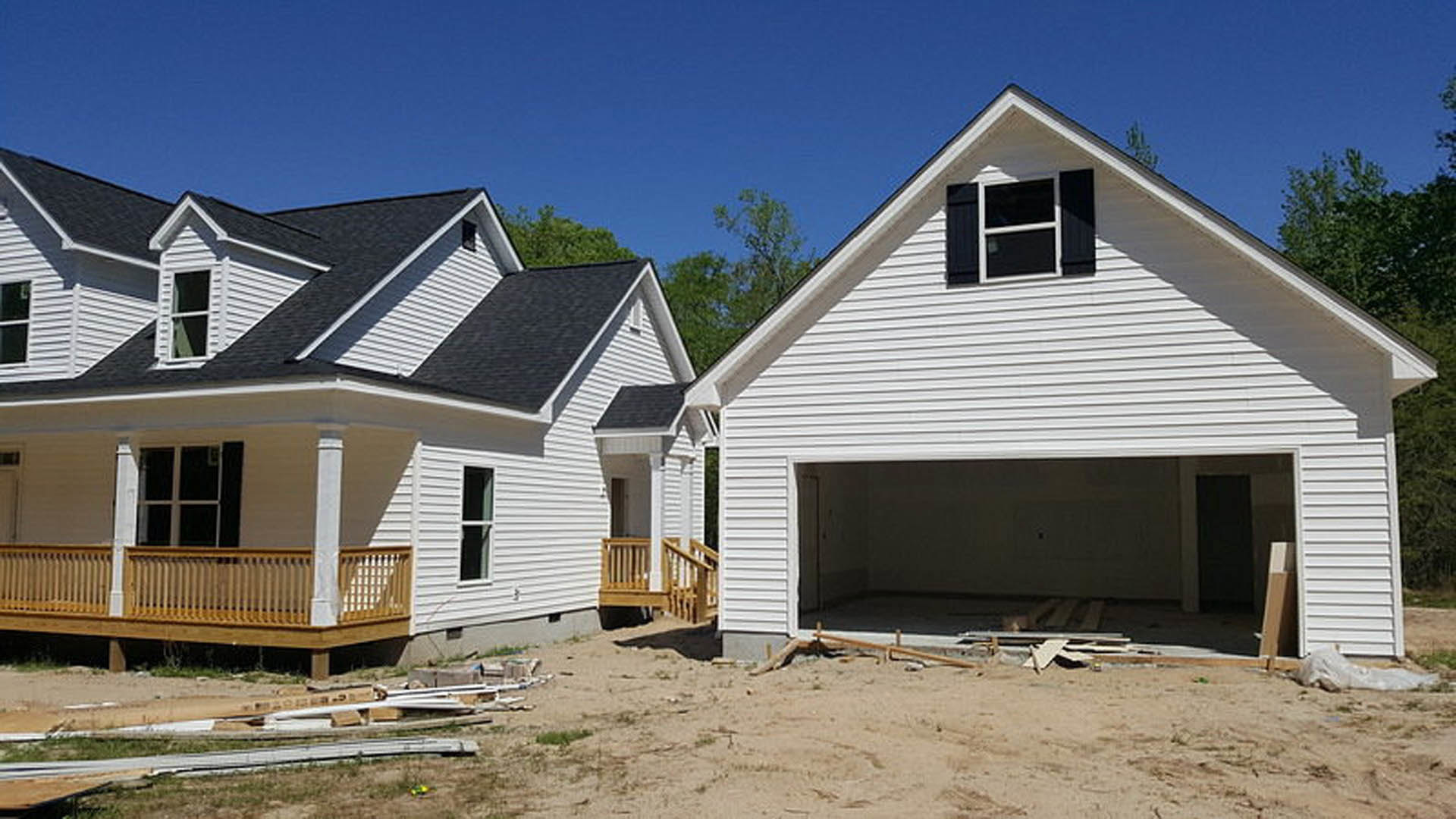 Two-story home under construction with attached garage, wooden porch railing, white-framed windows, and unfinished siding.