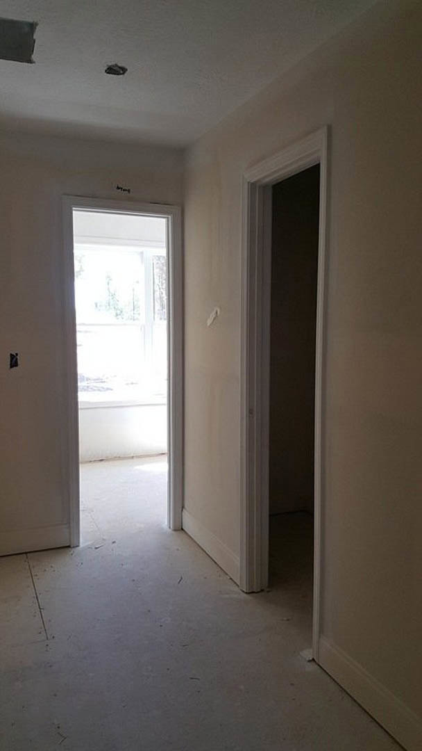 White plaster walls and light wood flooring frame a doorway with a window, revealing a snowy landscape outside.