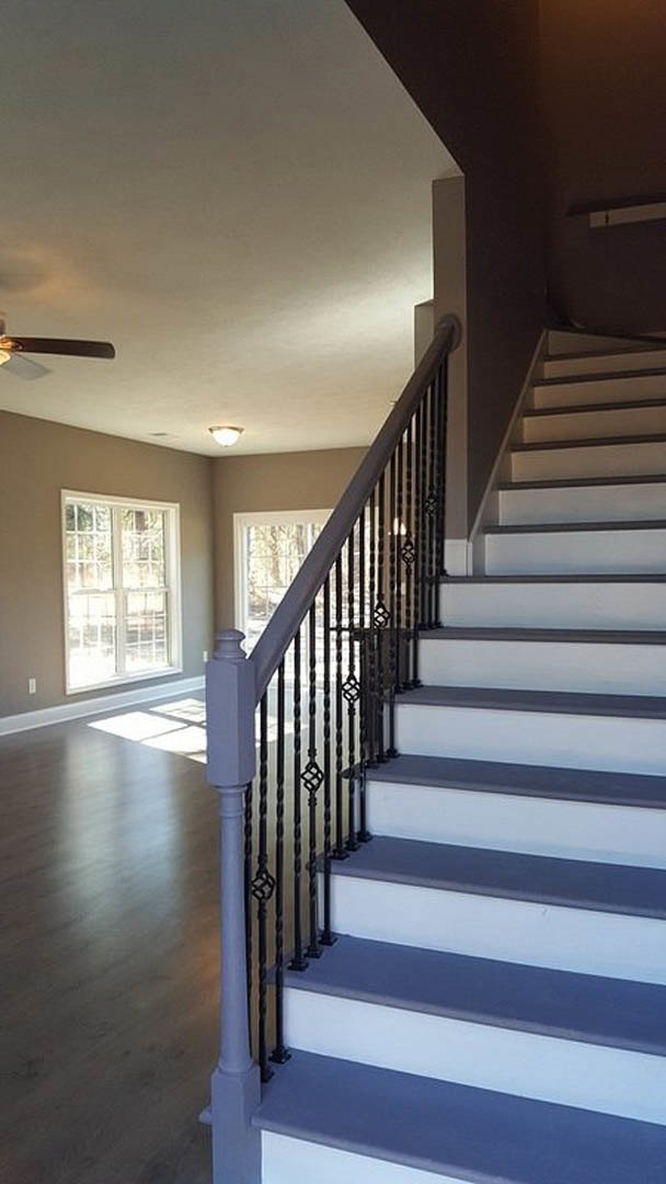 Wooden staircase with metal railing, light hardwood flooring, large window overlooking trees, white walls, and modern interior finishes