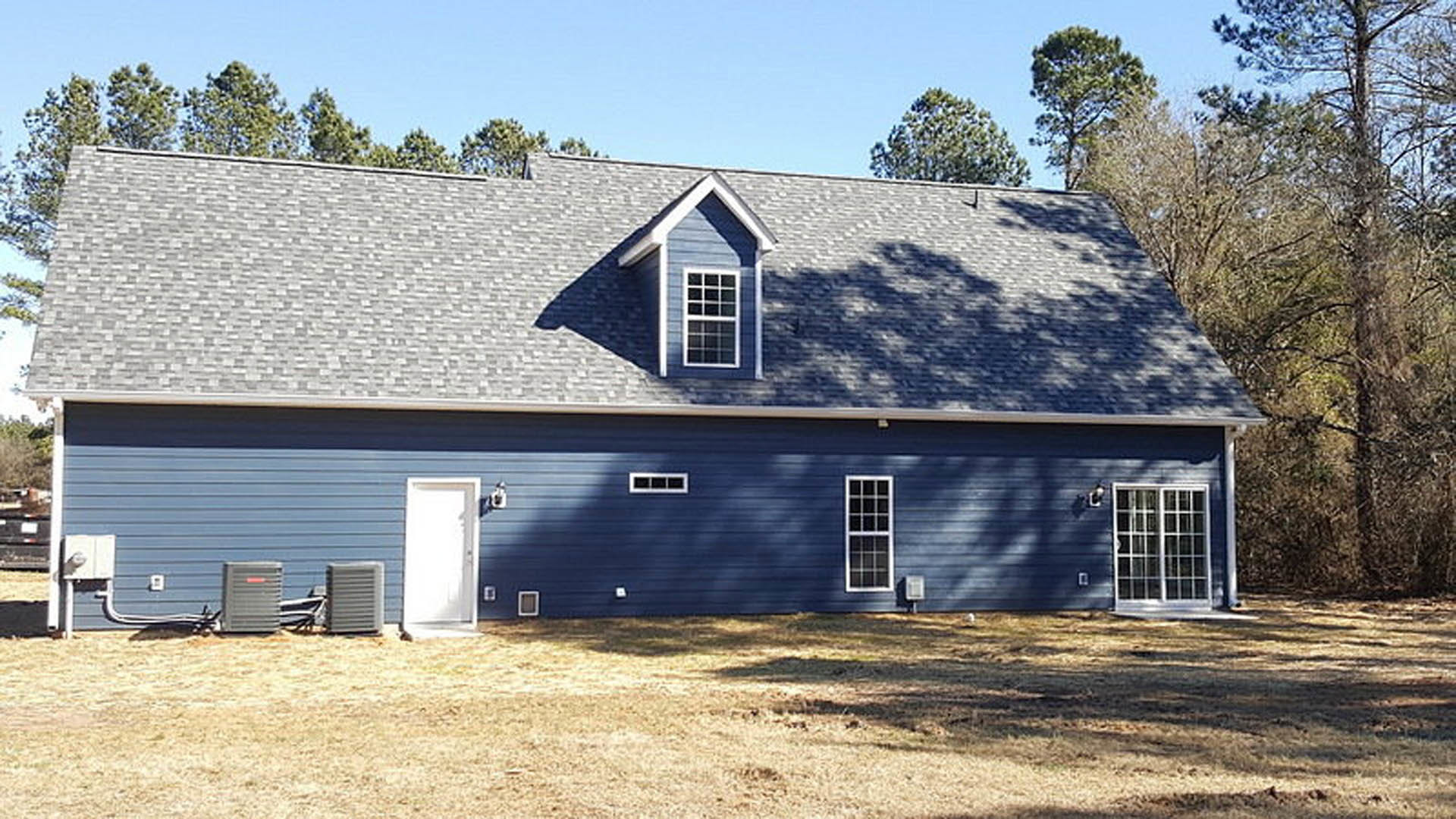 Blue siding home with white front door, multi-pane window, and tree in front yard under clear sky