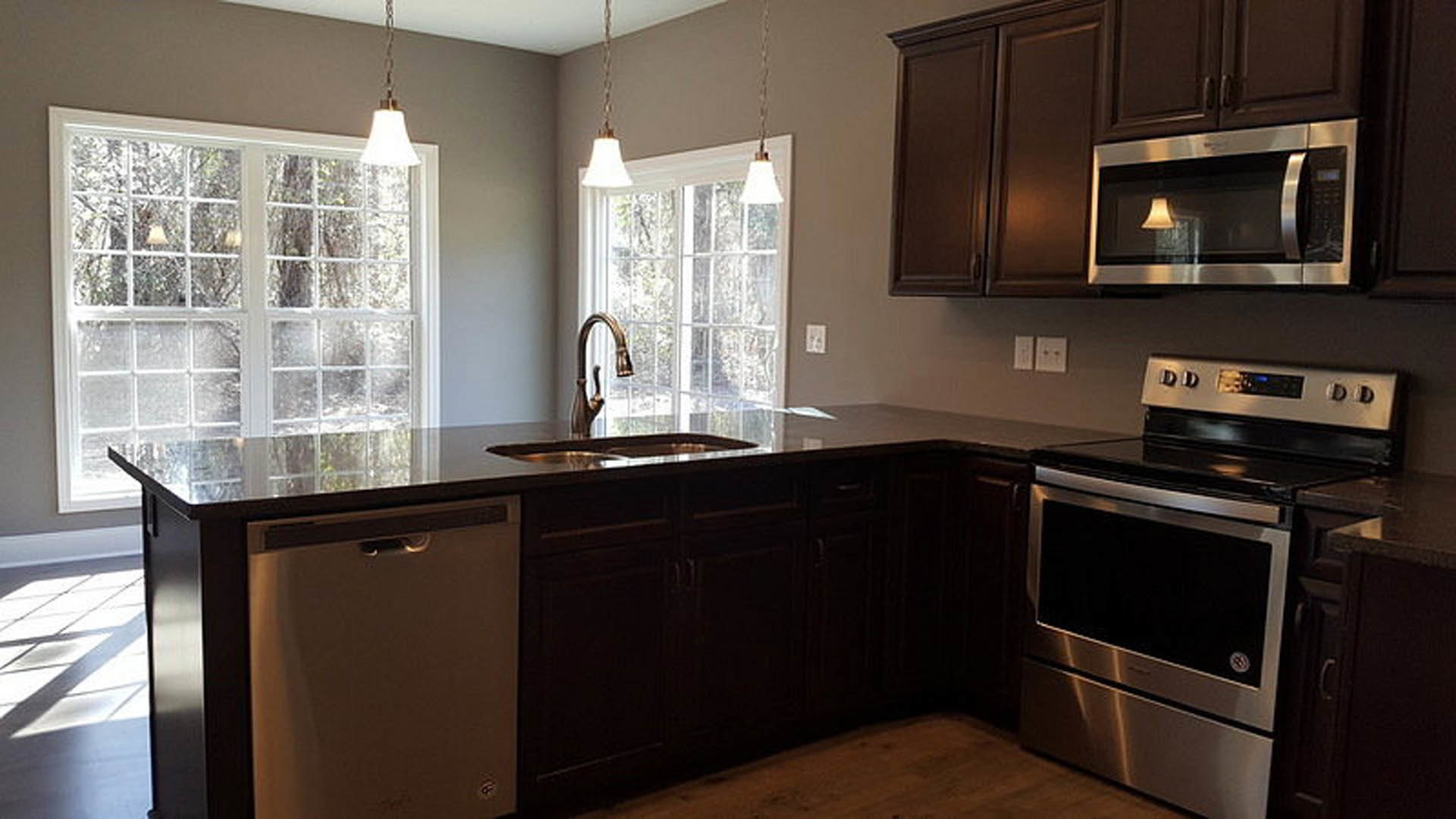 White kitchen cabinets and gray stone countertops with stainless steel refrigerator, oven, microwave, and sink; modern tile backsplash and brushed metal hardware.