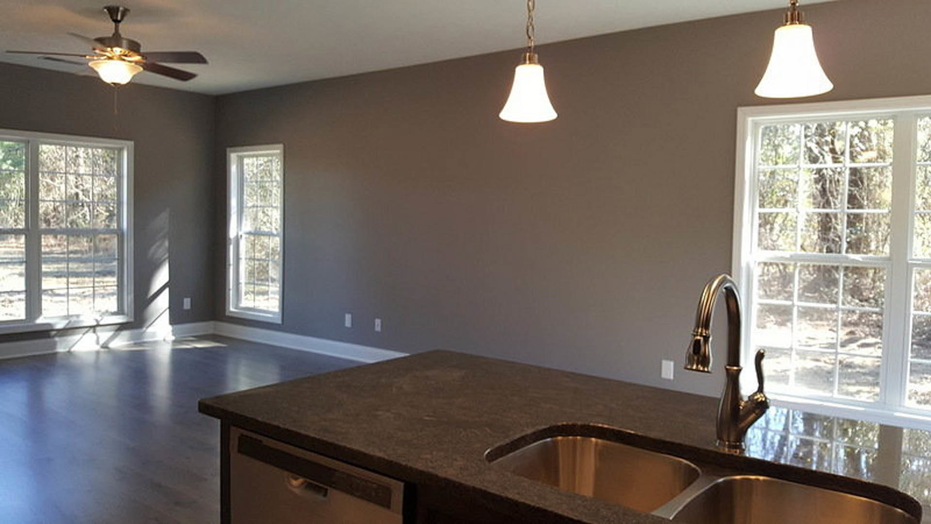 Modern kitchen featuring two stainless steel sinks set in a stone countertop, white cabinetry, large window with outdoor view, ceiling fan with integrated light, and sleek drawer