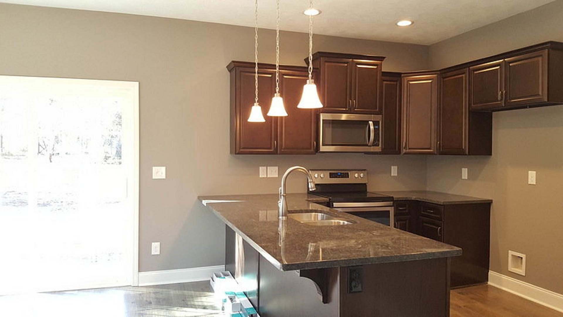Open-concept kitchen featuring a central island with pendant lights, white cabinetry, stainless steel microwave and stove, quartz countertops, undermount sink, and modern light