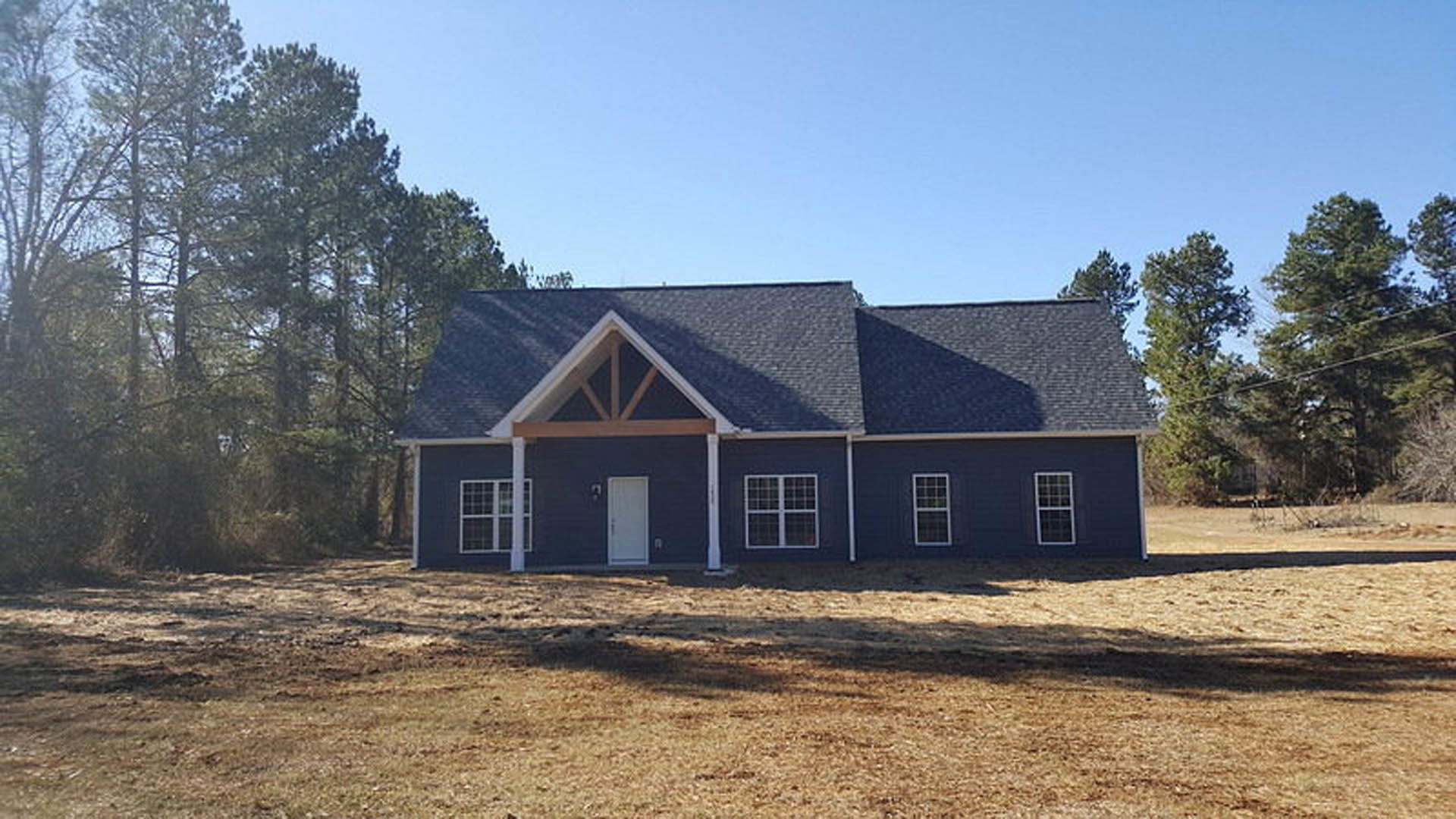 Blue metal roof on a modern cottage-style home, white siding, black-framed windows, white front door, manicured lawn, mature trees, clear sky
