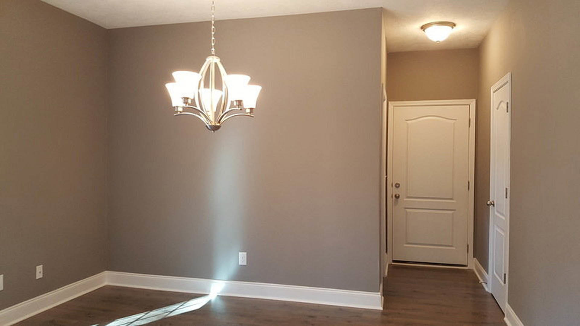 Chandelier with multiple lights hanging from white plaster ceiling, white door with silver handle, laminate flooring, and decorative molding along walls