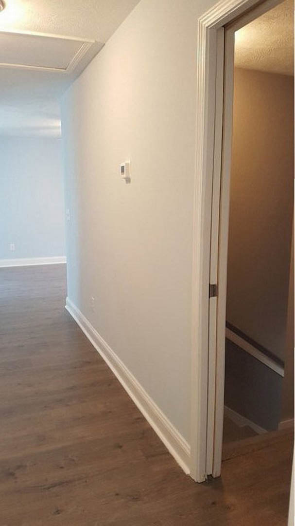 Hallway with open door, wood flooring, white plaster walls, black trim, visible thermostat