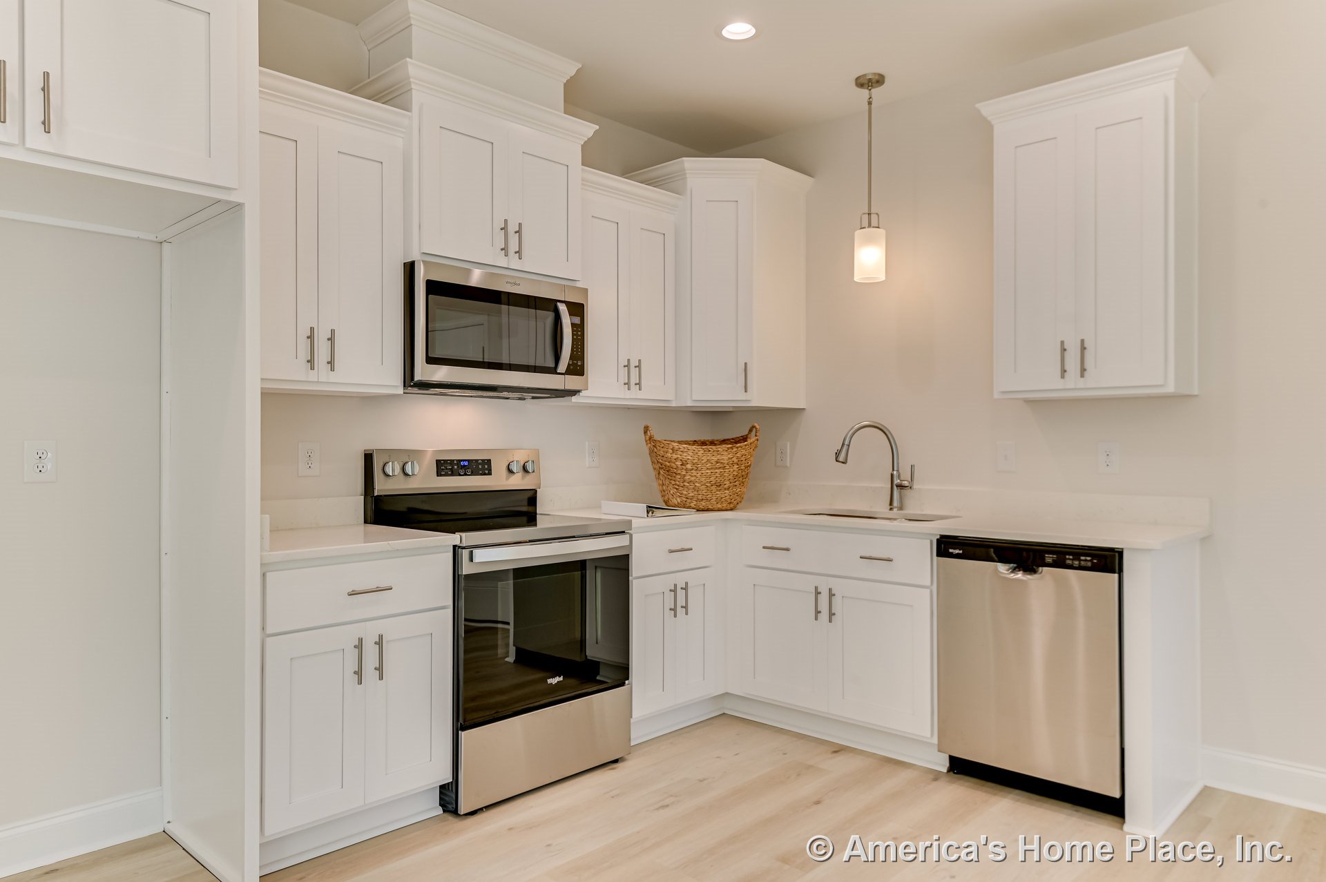 White shaker cabinets with stainless steel oven, microwave, and dishwasher, quartz countertops, single bowl undermount sink, pendant ceiling light, and light wood plank flooring.