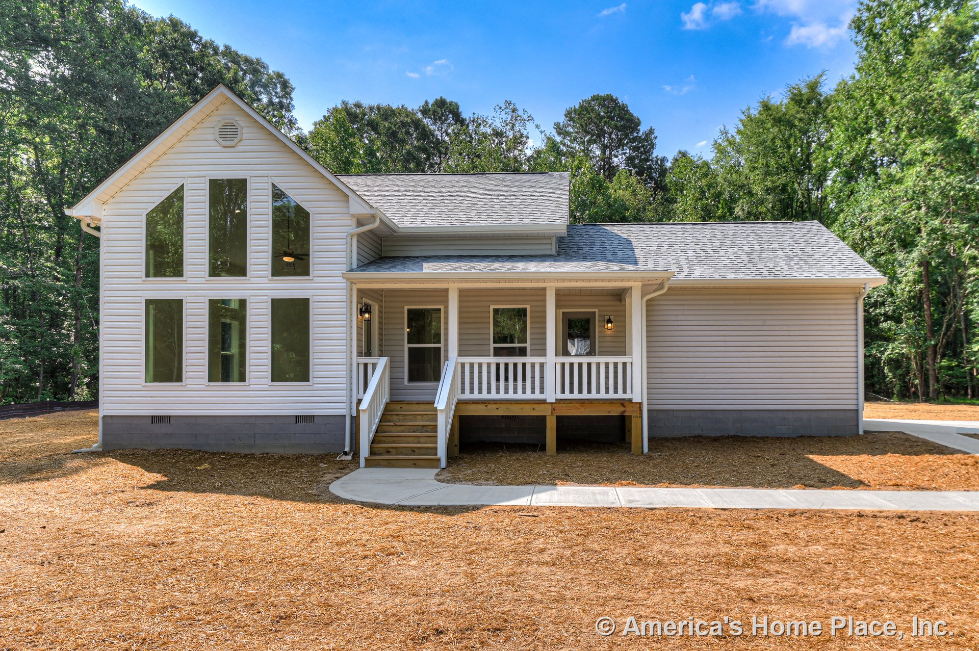 Covered front porch with white railings, large vertical windows on the left, gray shingle gabled roof, vinyl siding exterior, concrete walkway and steps leading to entry door